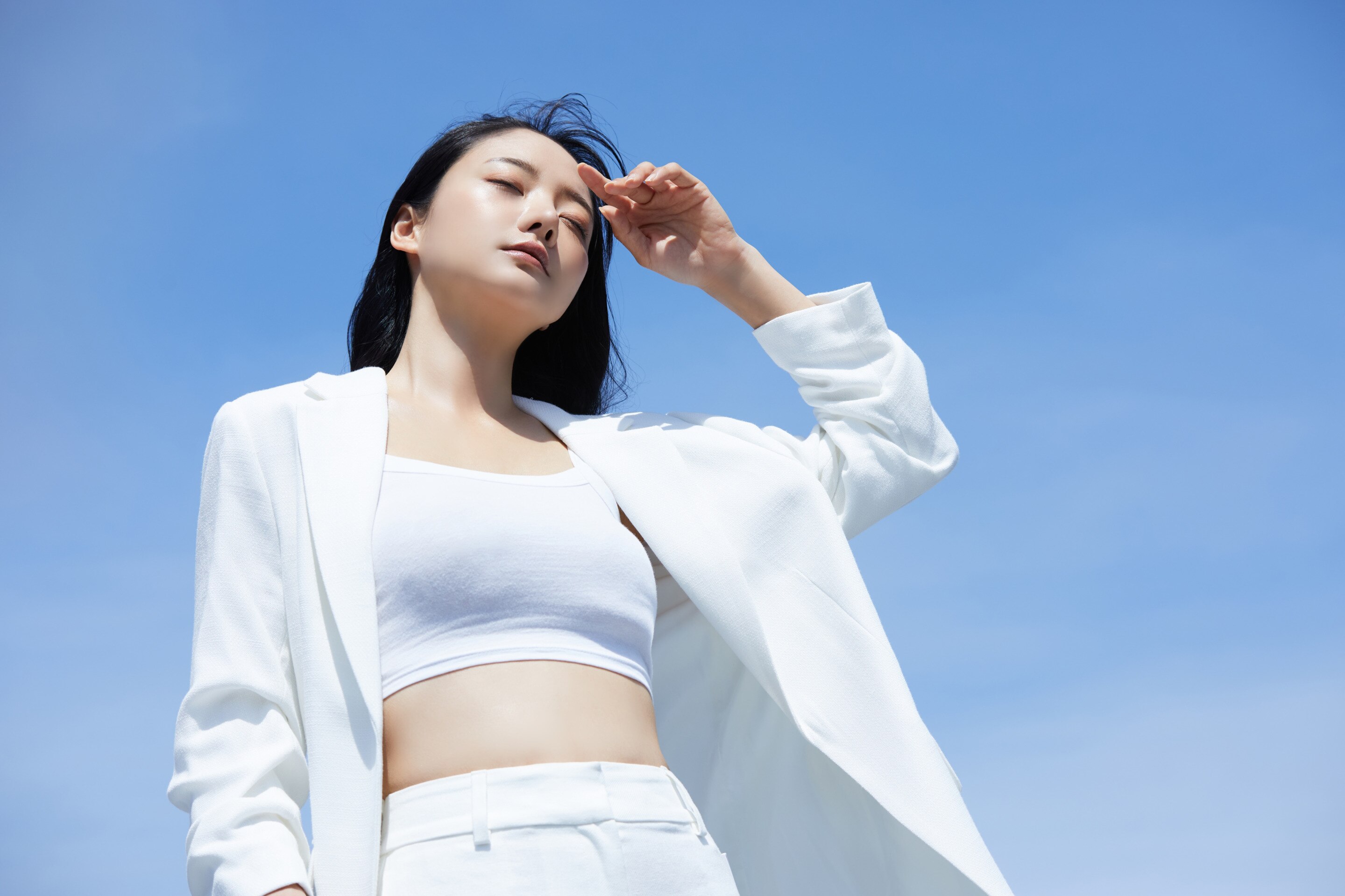 ada wanita asia yang sedang berada di luar ruangan dan menahan panas matahari dengan tangan