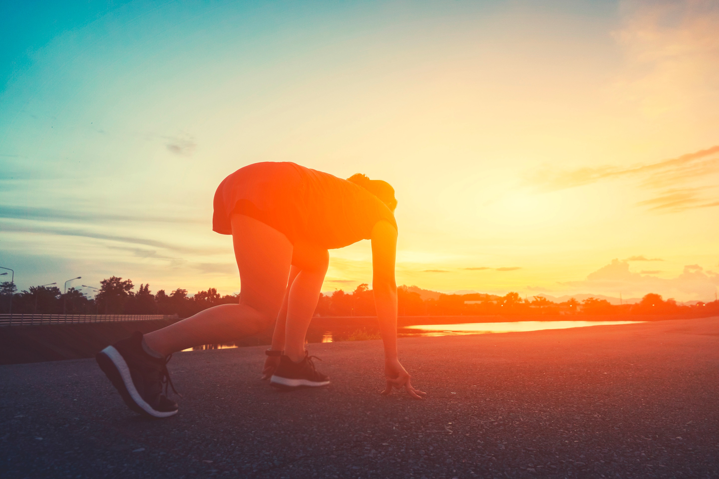 seorang wanita sedang dalam posisi start lari di atas jalan terbuka.