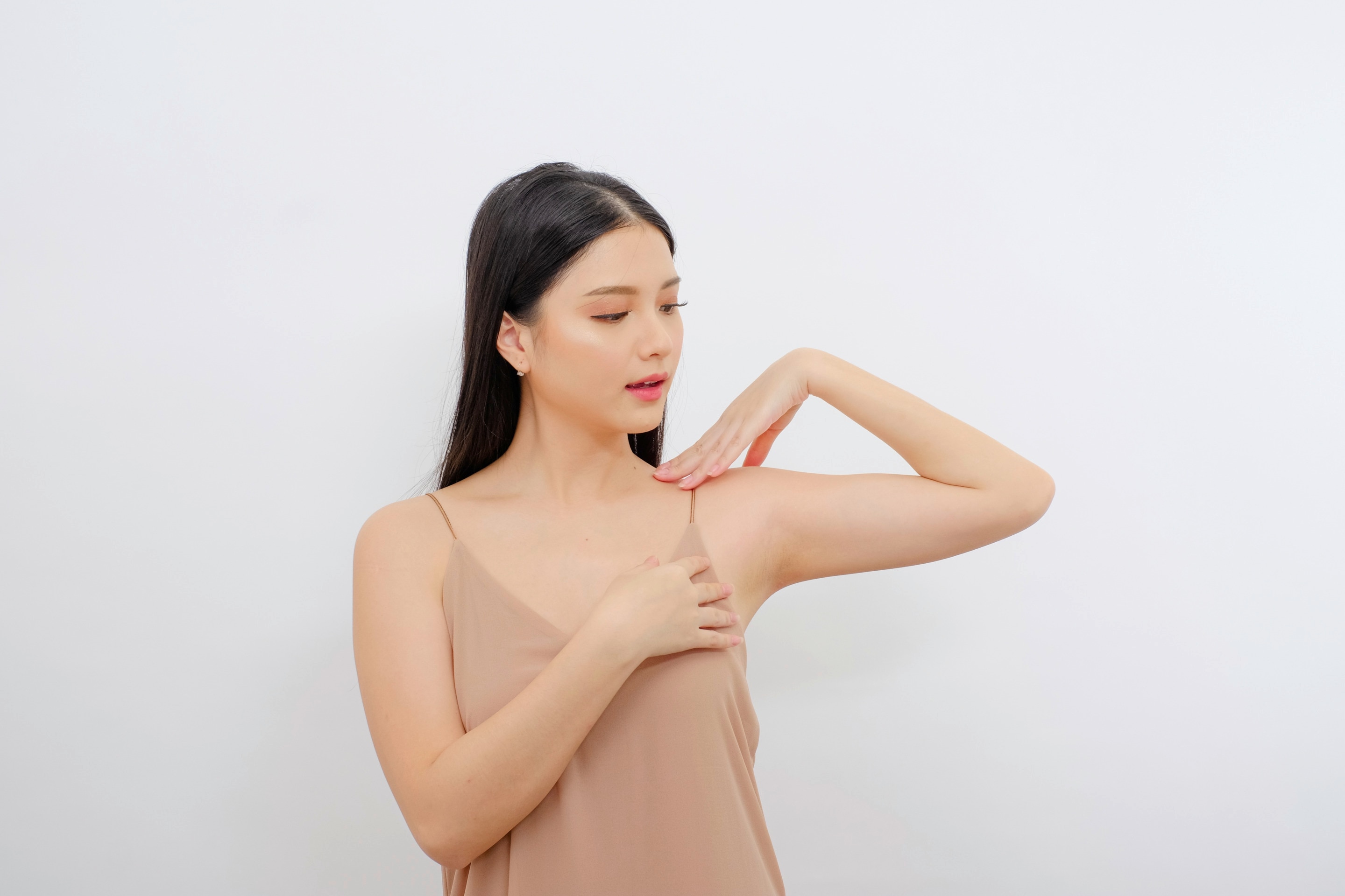 seorang wanita mengenakan tank top berwarna nude sedang mengangkat lengannya dan memperhatikan area ketiak.