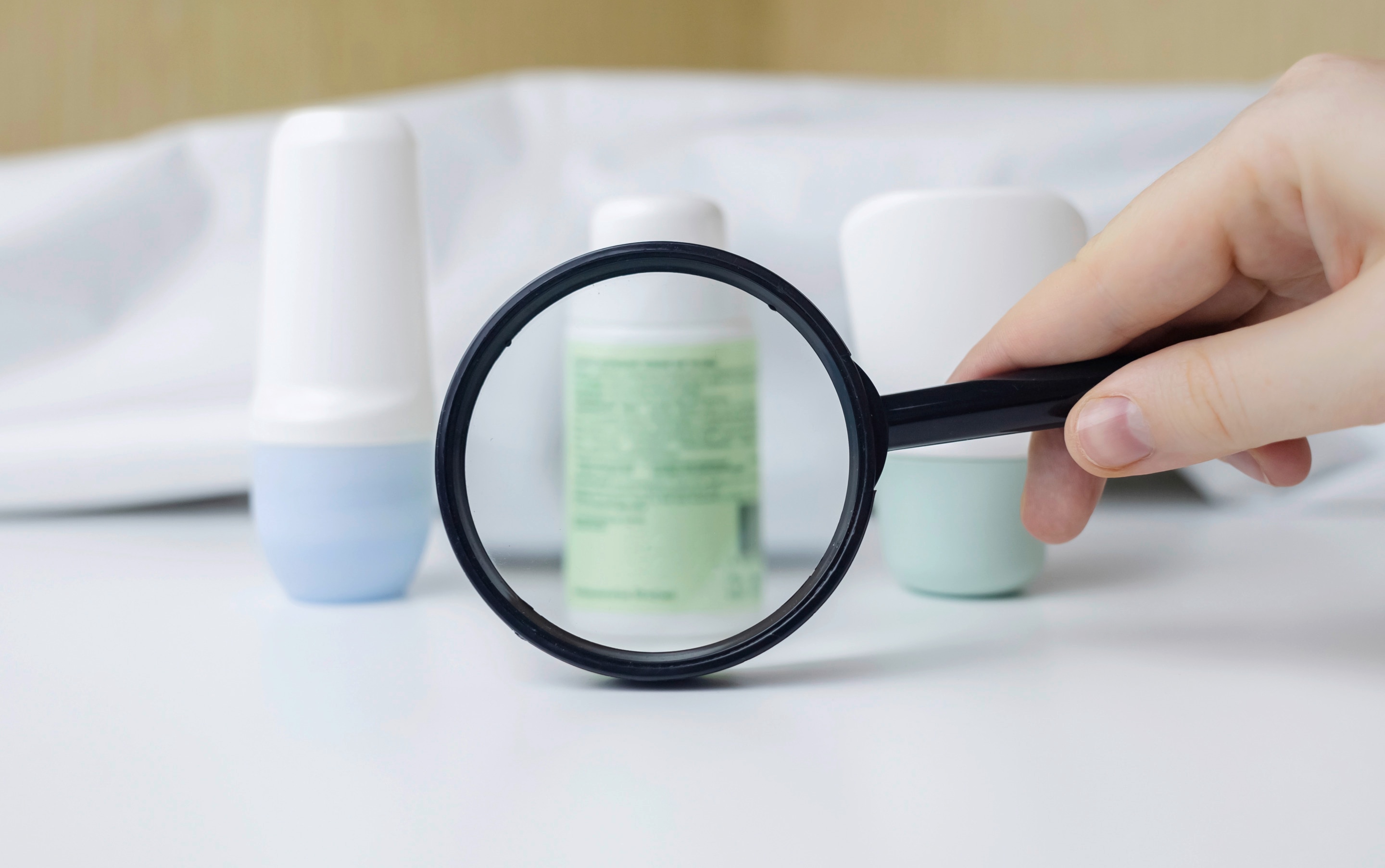 tangan sedang memegang kaca pembesar untuk melihat produk deodorant yang diletakkan di atas meja