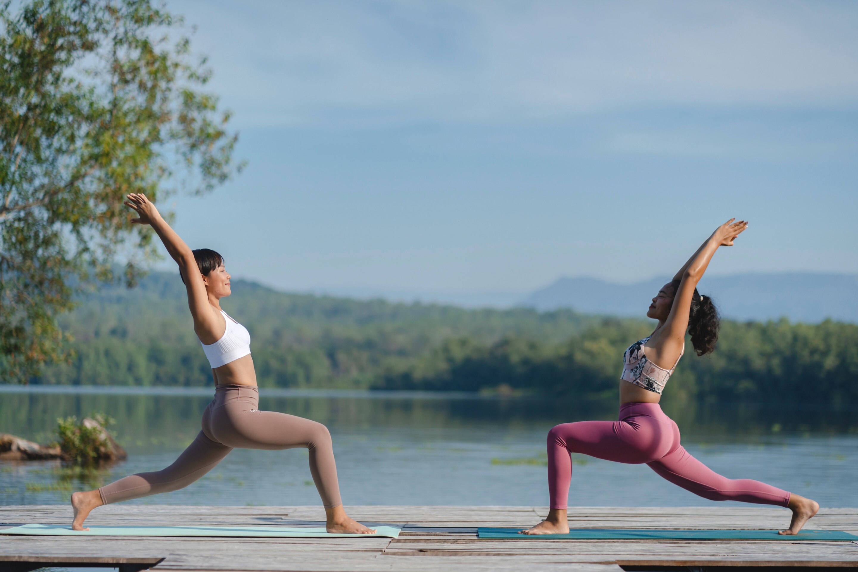Two women practicing yoga by a lake.