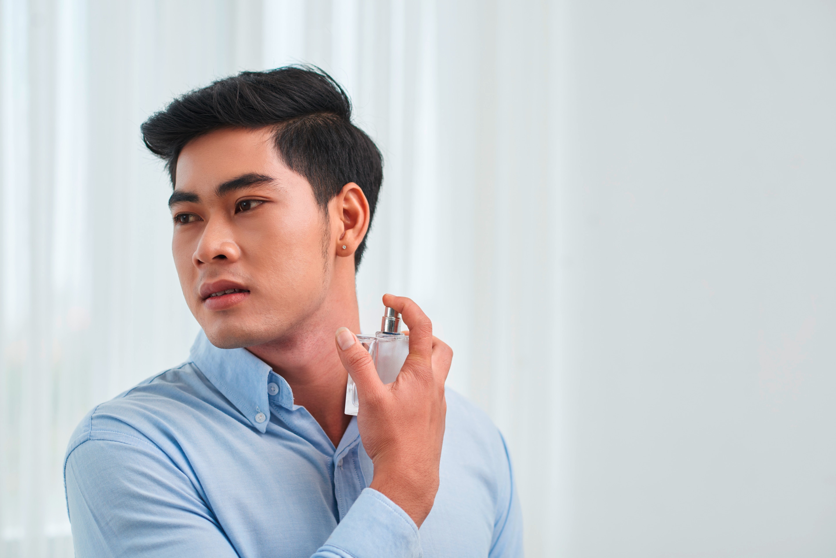 Asian man spraying cologne on his neck.