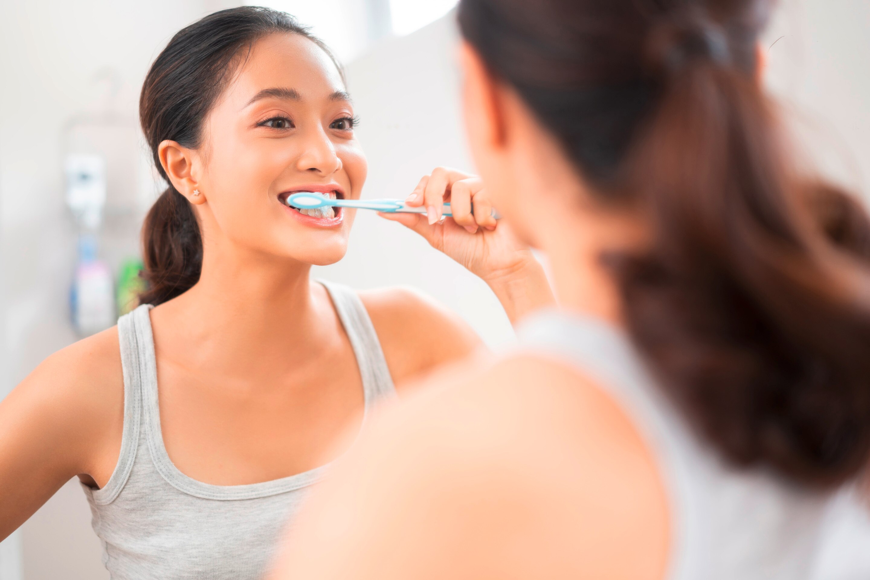 A woman is brushing her teeth in front of the mirror..
