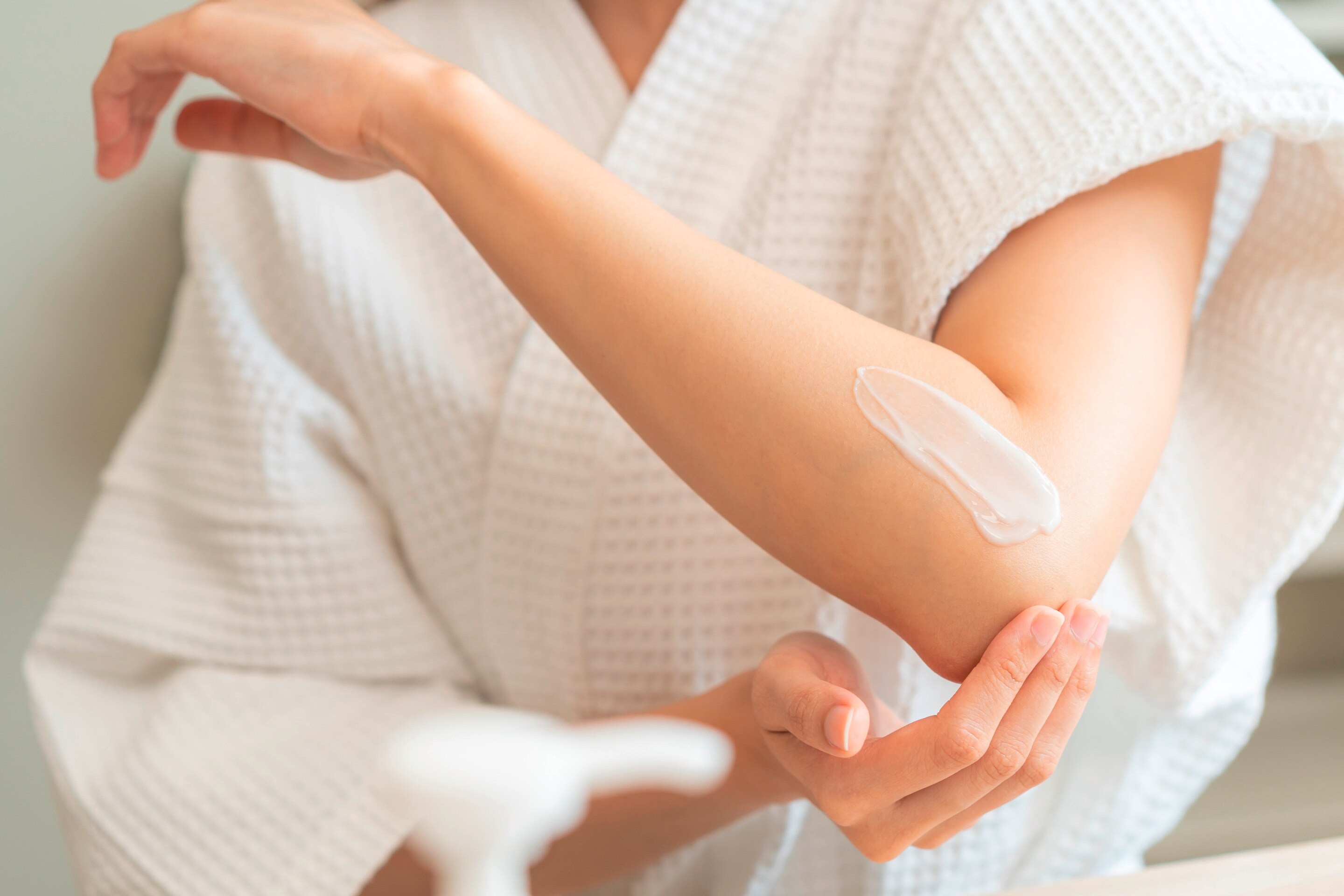 A young woman applies lotion on her arms after her shower.
