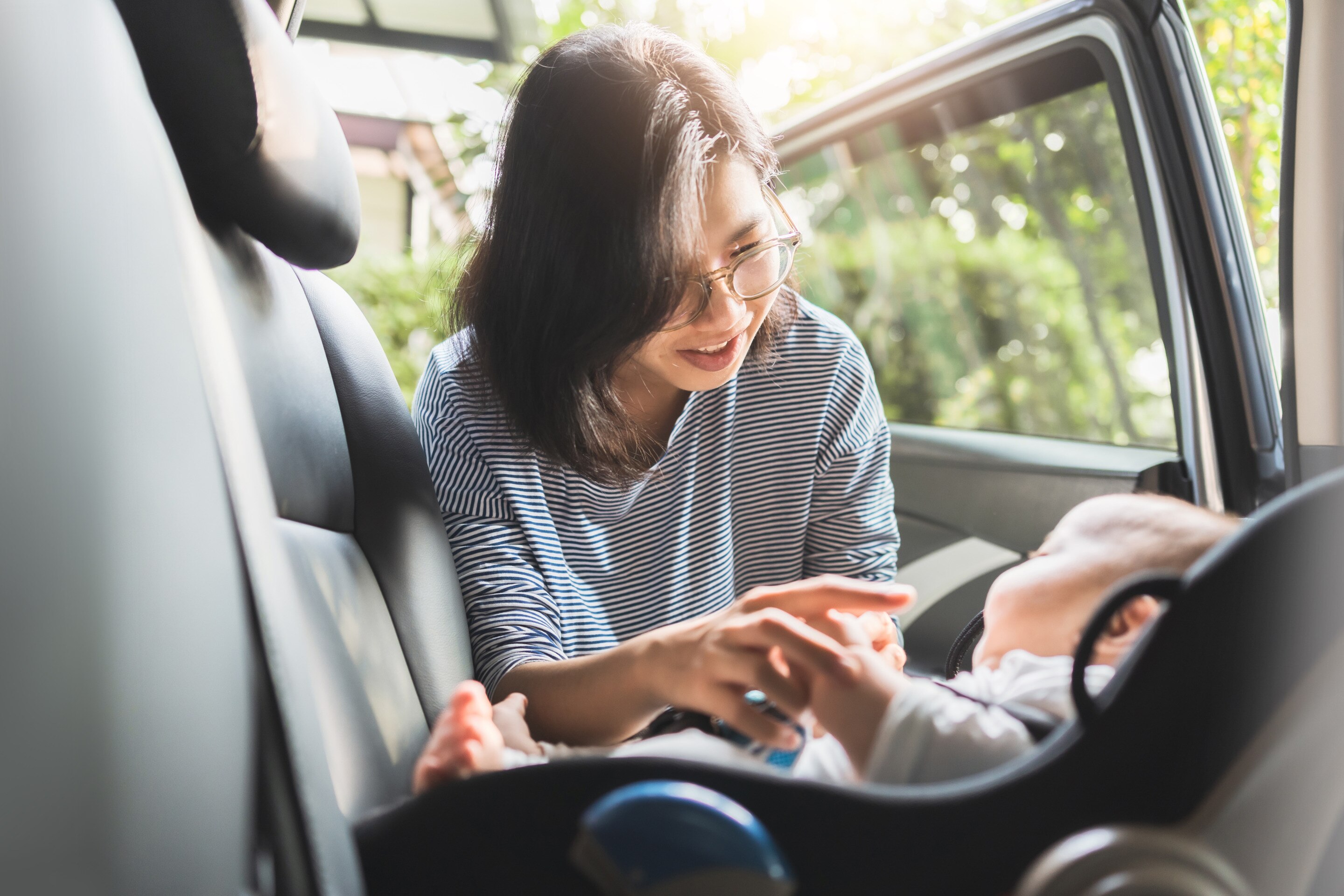 ada ibu tersenyum berinteraksi dengan bayi di car seat saat perjalanan mudik bersama bayi.