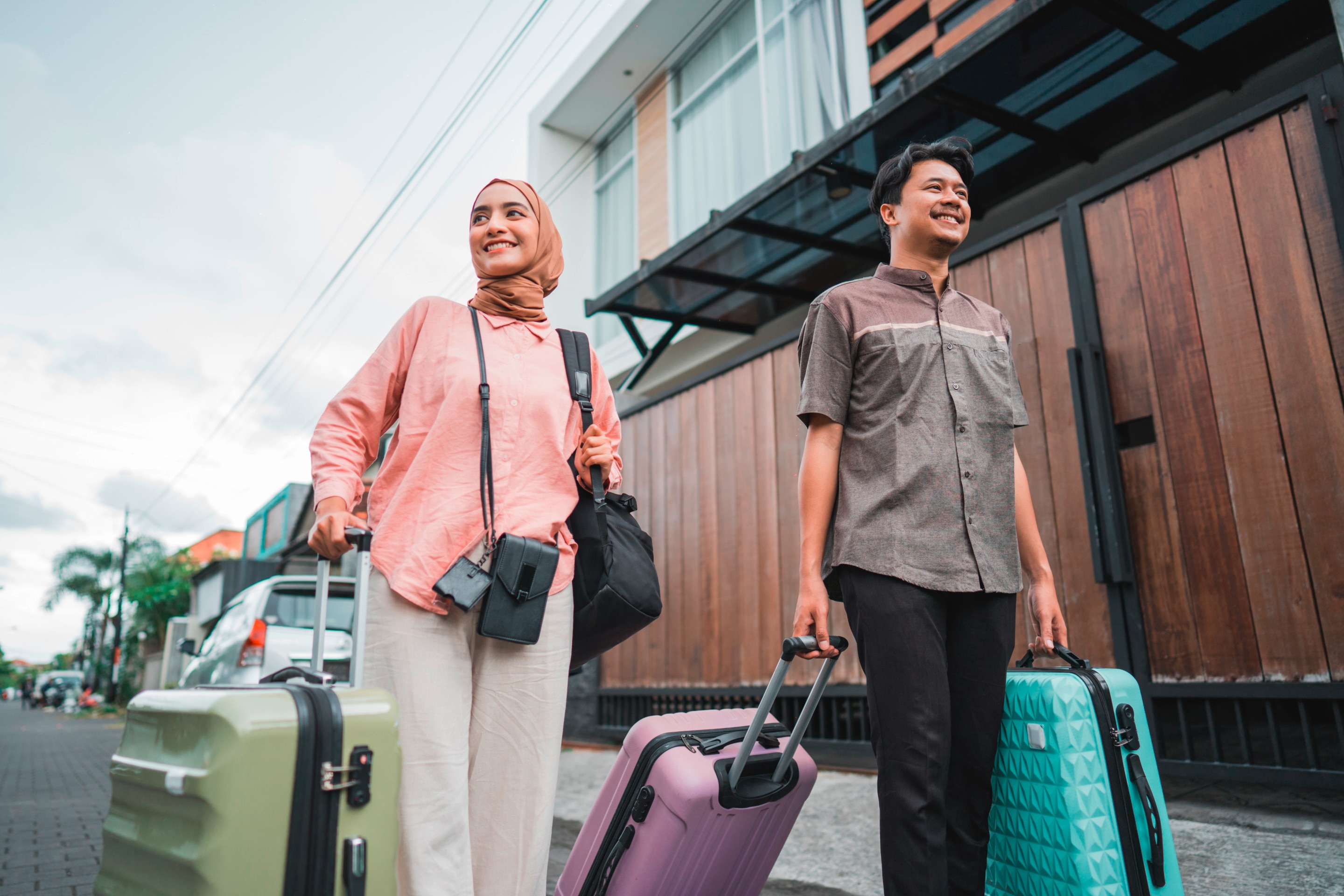 ada pria ada wanita berhijab sedang menenteng koper dan tas untuk mudik