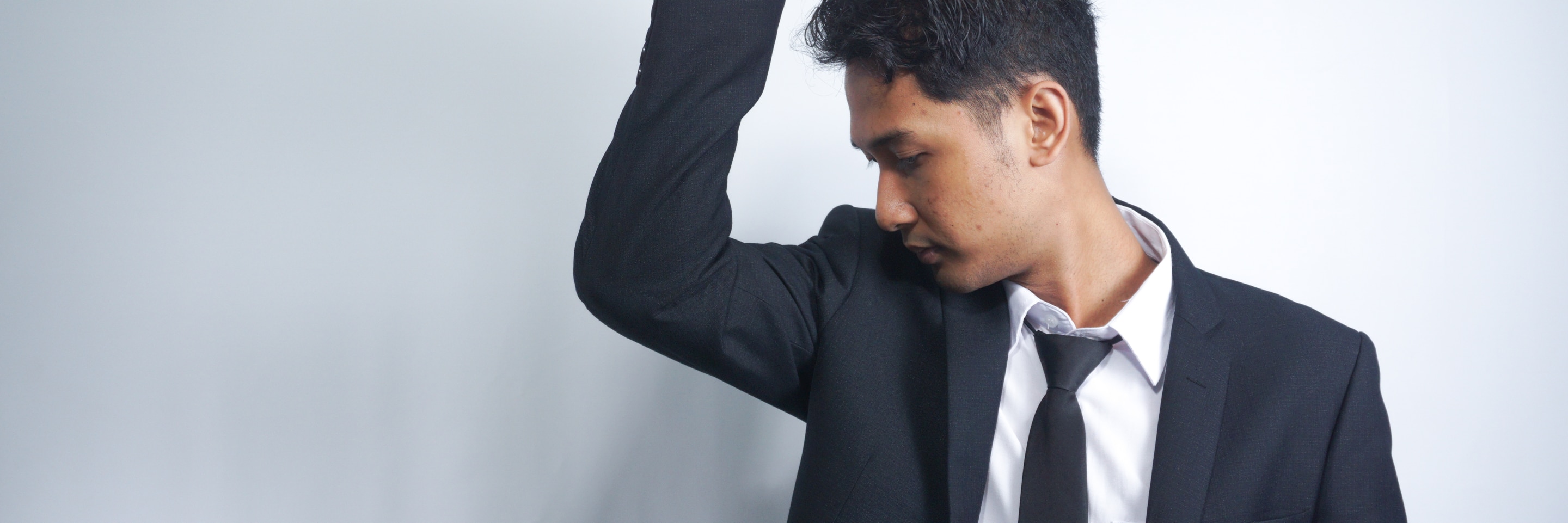 Man in a suit raising his arm and looking down at his underarm, as if checking for odor or sweat 