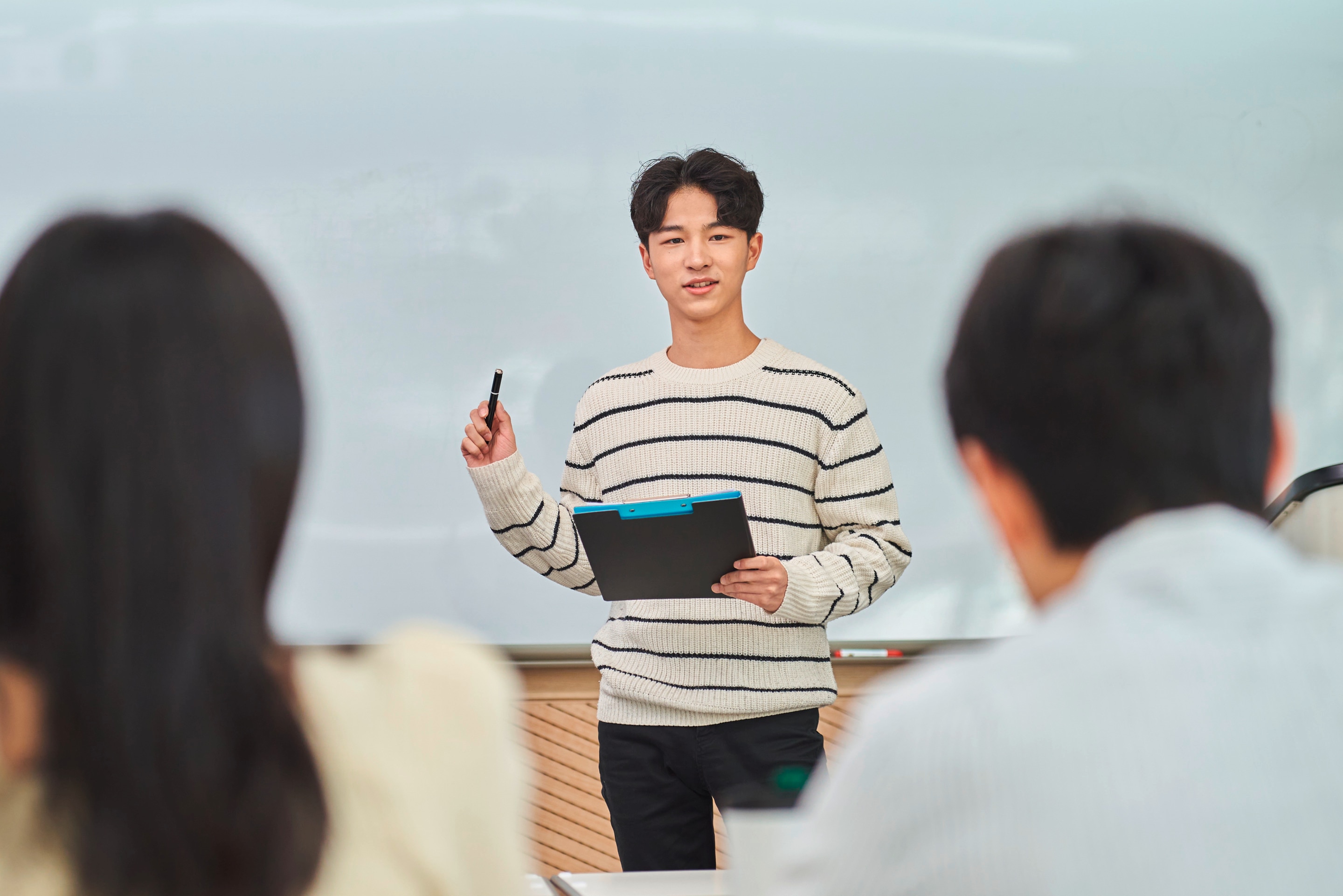 pria Asia sedang tersenyum percaya diri saat melakukan presentasi di kantor di depan banyak rekan kerja.