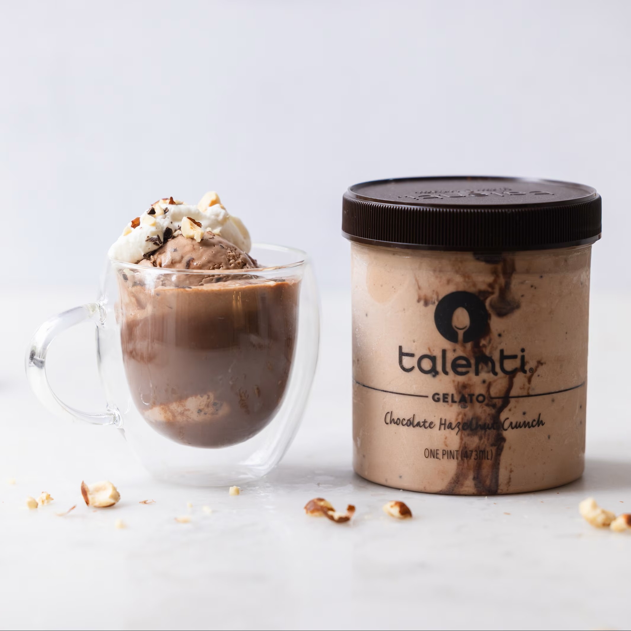 A Hot Chocolate Hazelnut Crunch Affogato in a clear mug with a pint of Talenti Chocolate Hazelnut Crunch Gelato next to it. 