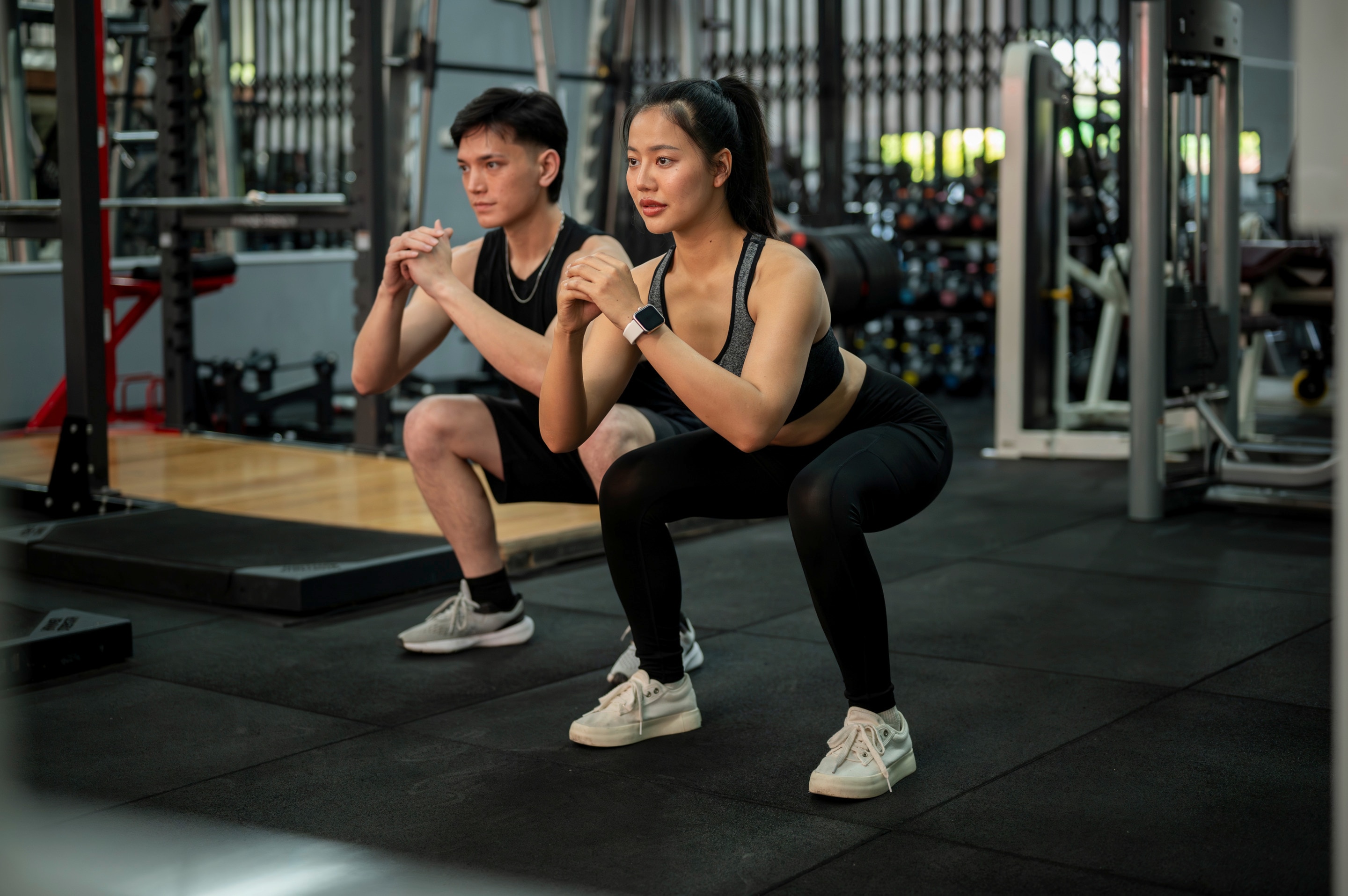 Seperti yang terlihat pada foto, ada pria dan wanita Asia sedang melakukan latihan daya tahan tubuh dengan gerakan squat.