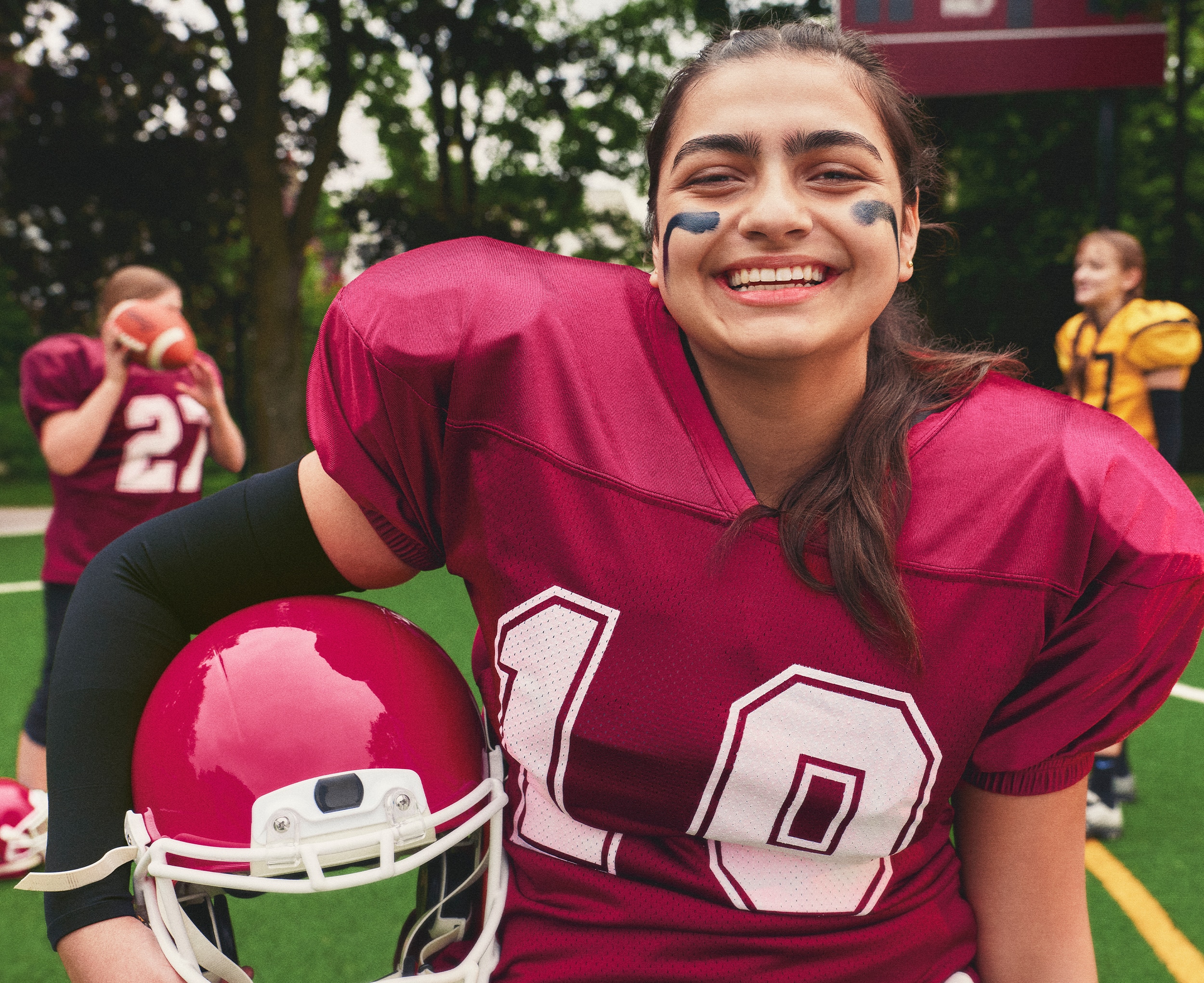 Girl smiling on a field holding a football helmet