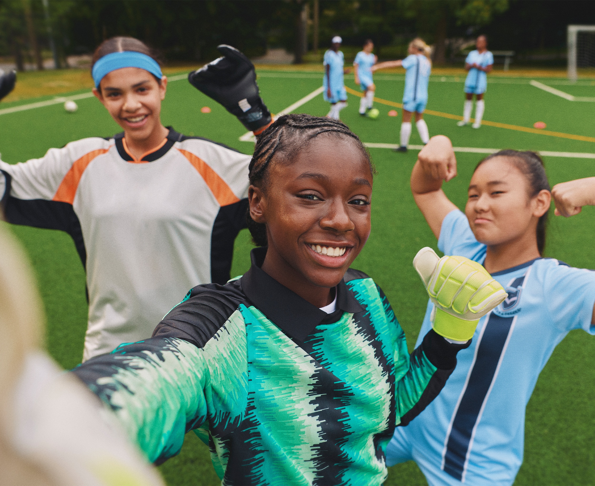 Three girls smiling taking a selfie together on a soccer pitch.