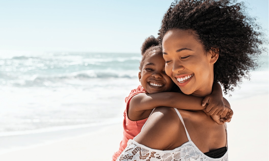 Woman on the beach carrying a child, looking happy and not worried if her deodorant has expired