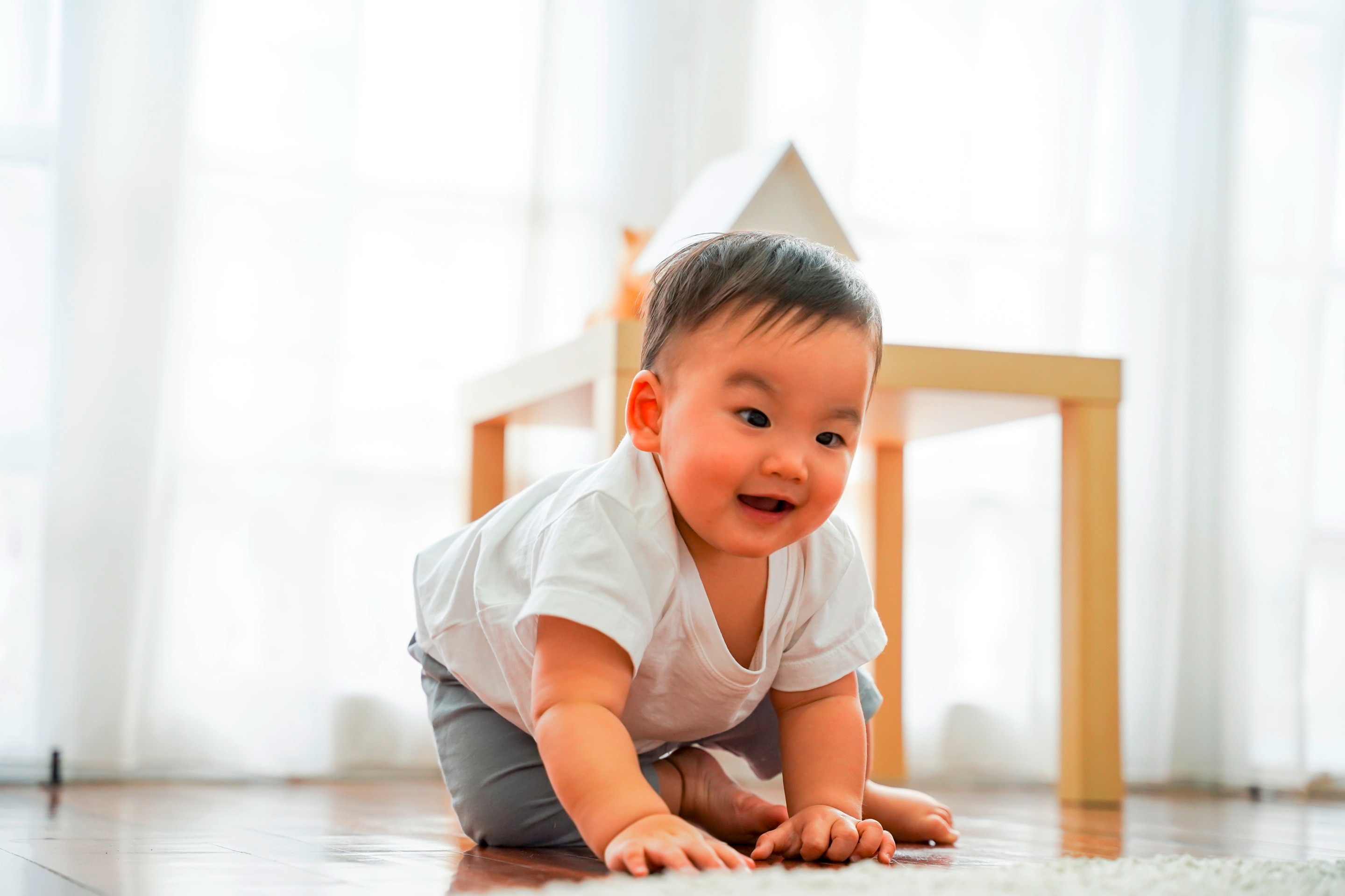 ada bayi merangkak di lantai saat bermain, salah satu tahap perkembangan sebelum bayi bisa duduk sendiri.