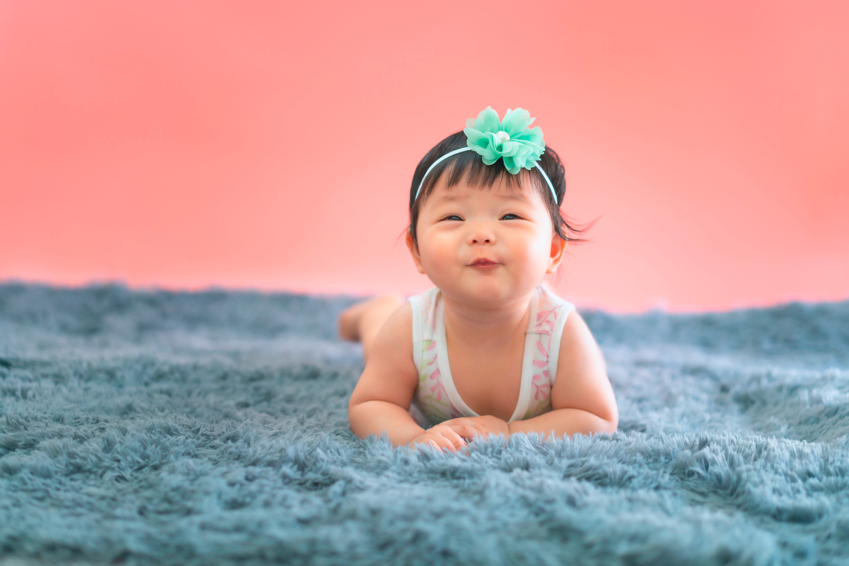 ada bayi usia 6 bulan yang sedang tengkurap dan tersenyum.