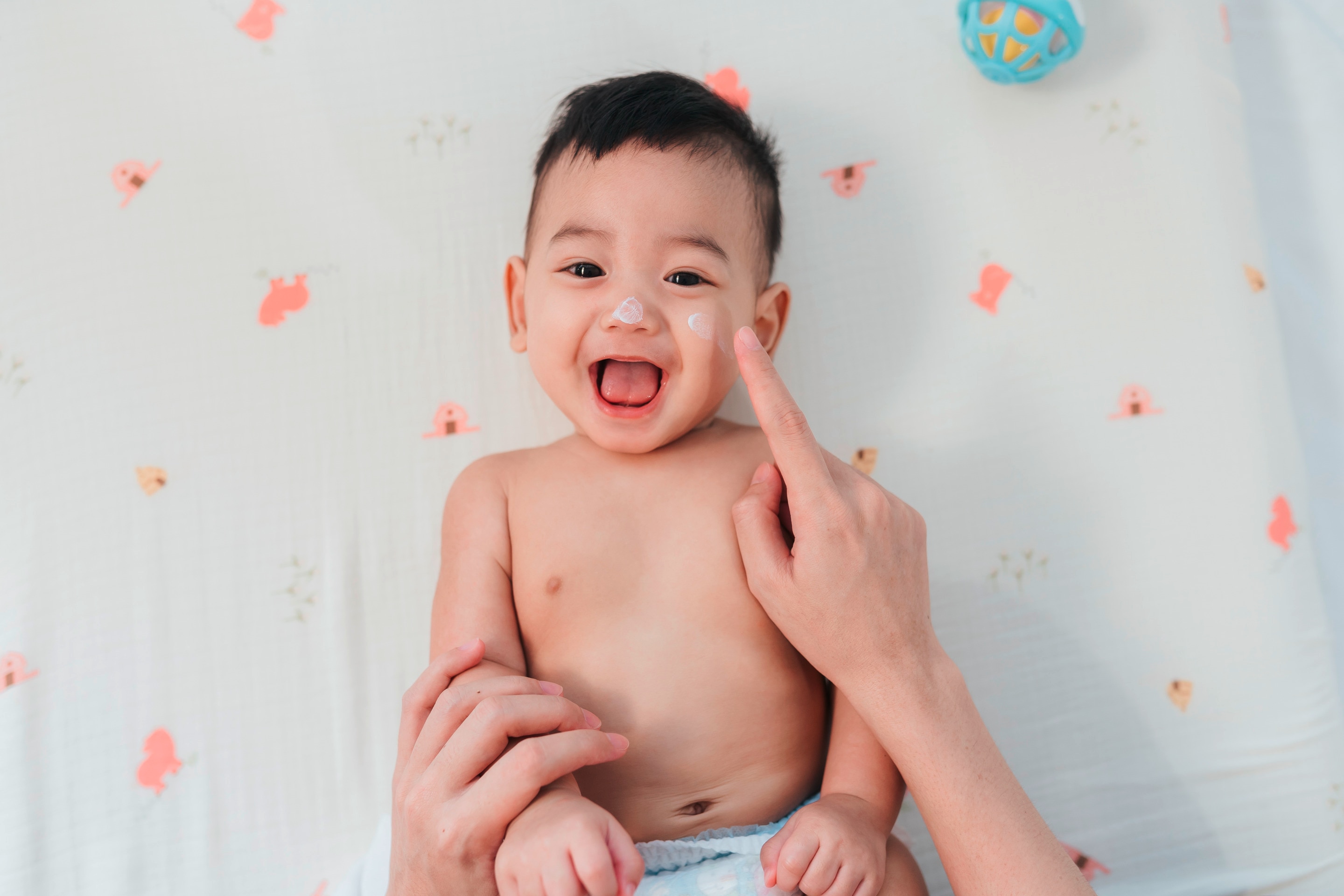bayi yang sedang dioleskan pelembap untuk kulit kering.