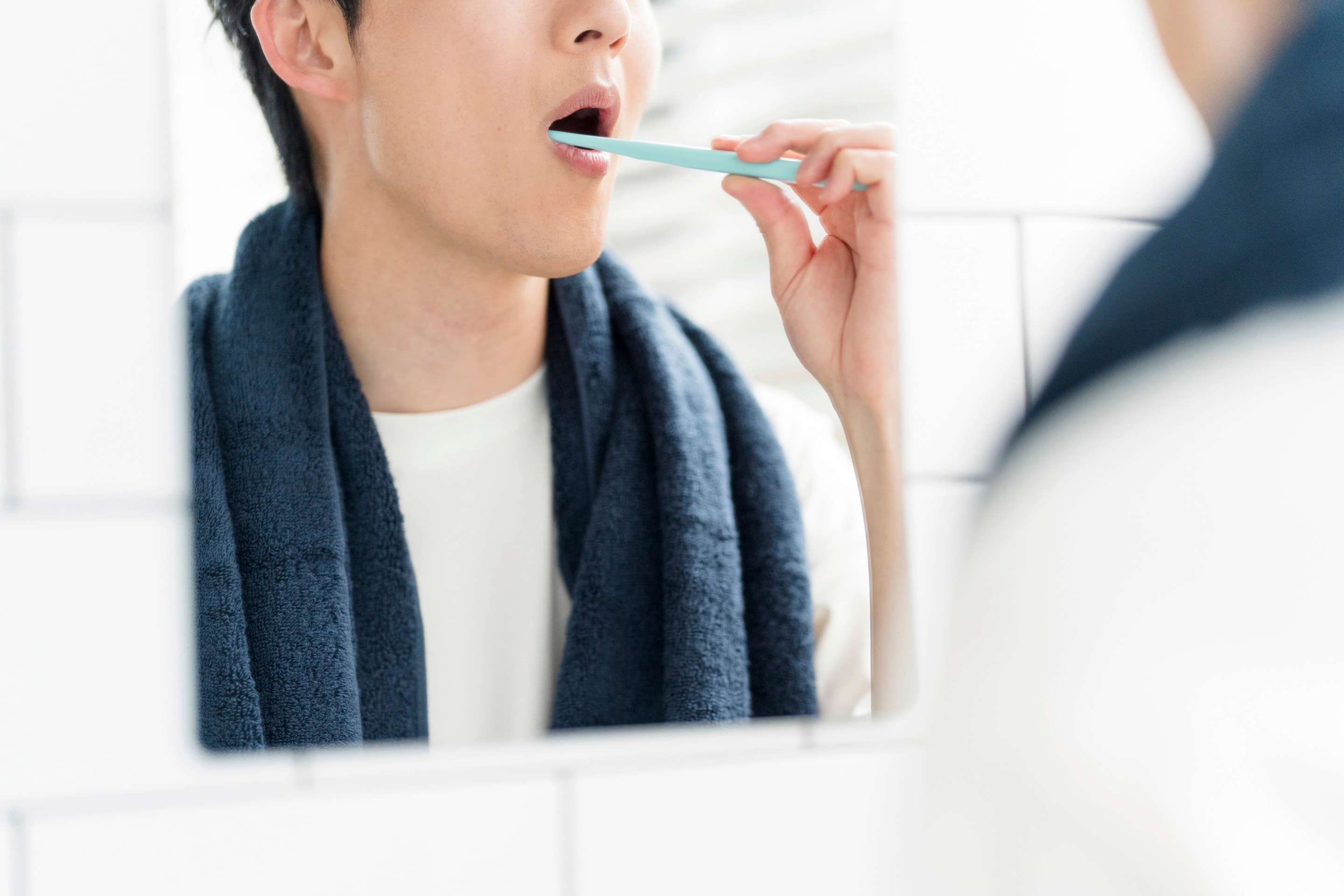 An Asian man brushes his teeth in front of the mirror. 