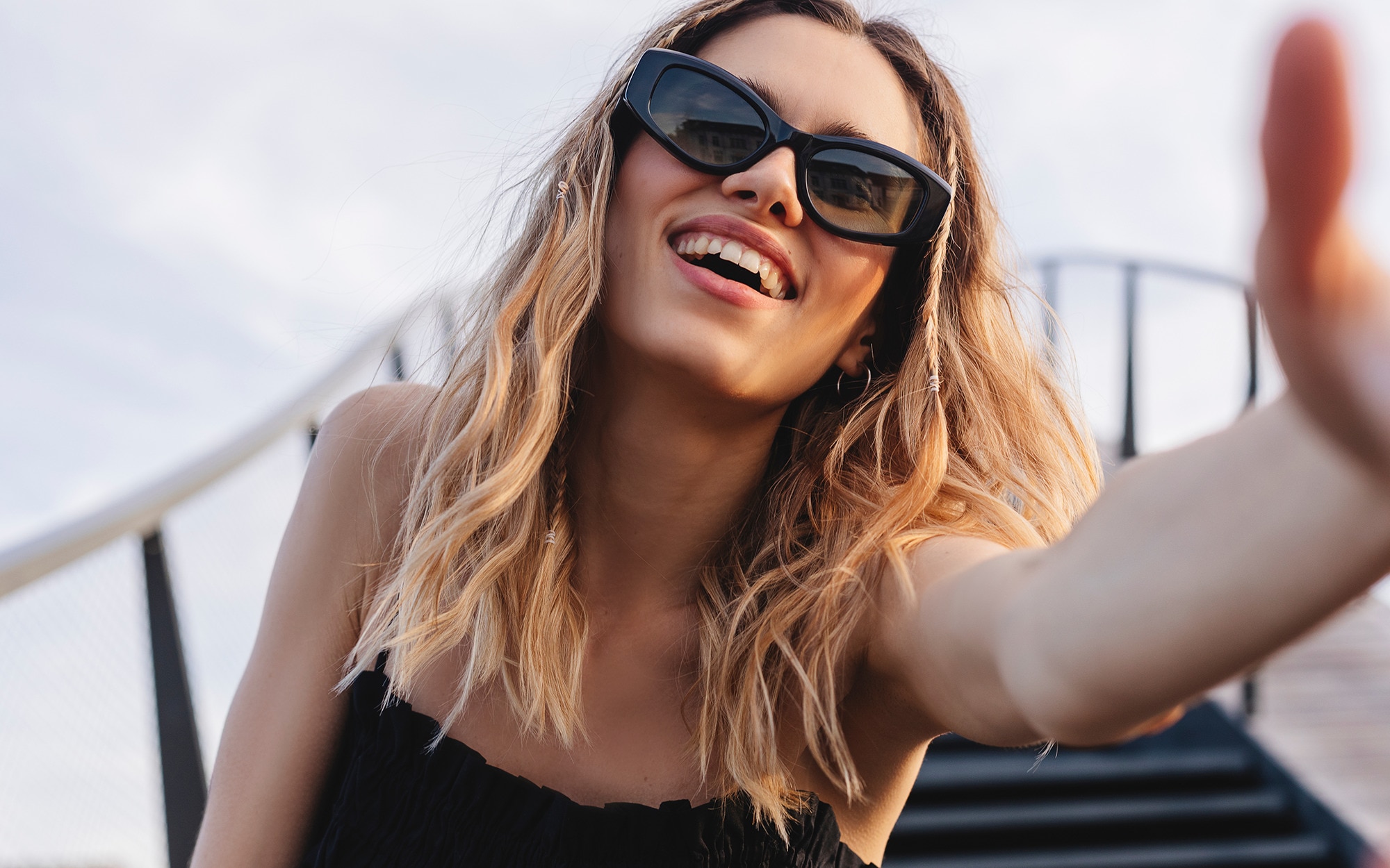 Woman with festival-ready hair in sunglasses laughing with stairs and sky in background