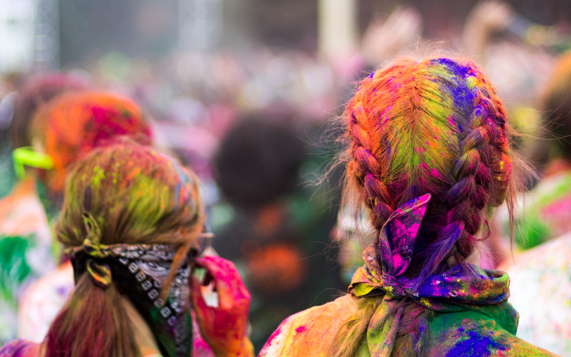 Back view of two female heads with loose Dutch braids covered in colourful paint powder at an outdoor festival