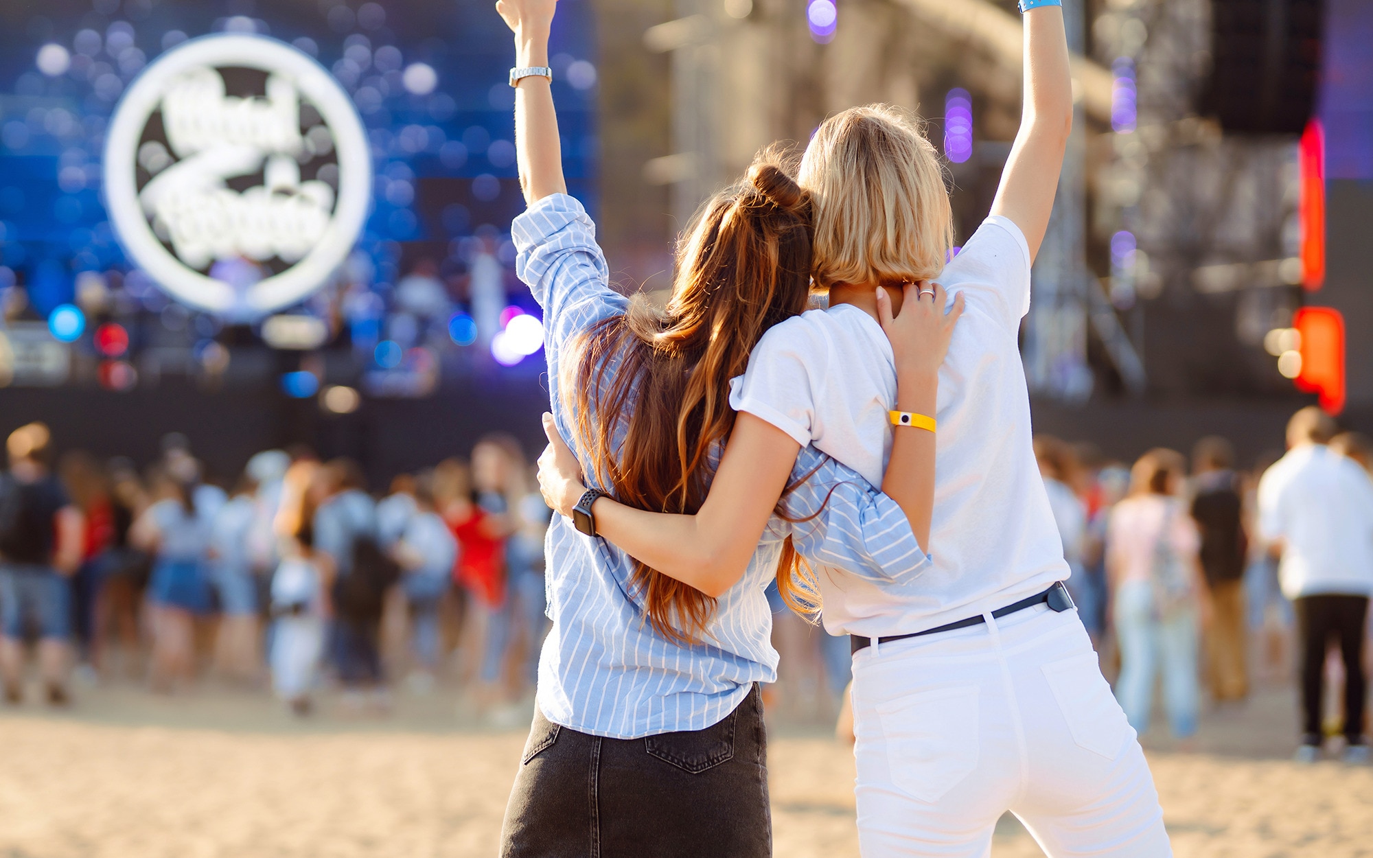 Back view of two women with half-up hairstyles celebrating at an open-air festival