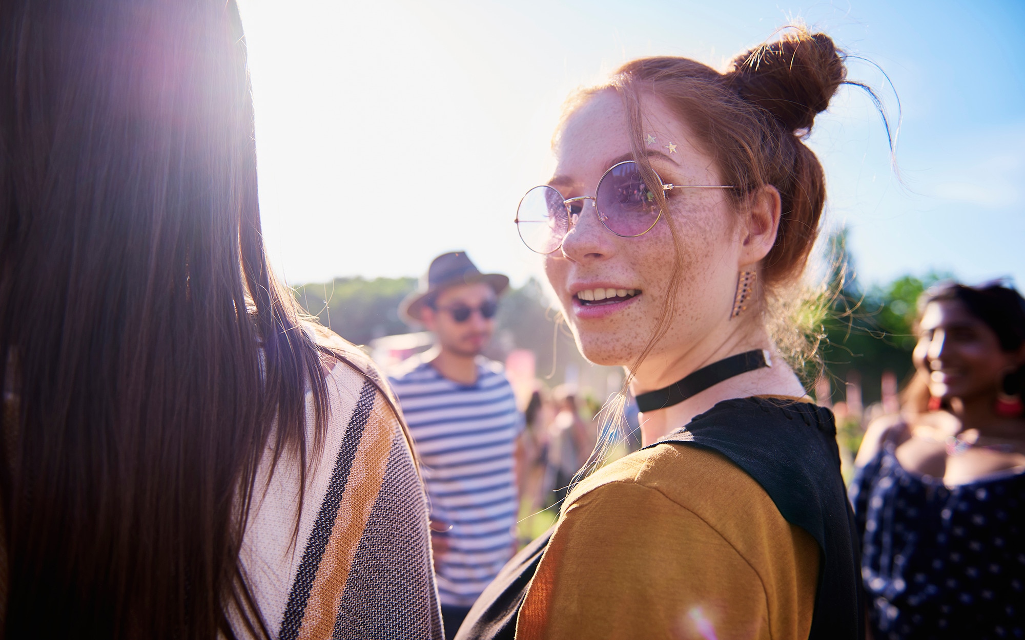 Woman wearing choker and two high buns at an outdoor music festival with blue sky in background