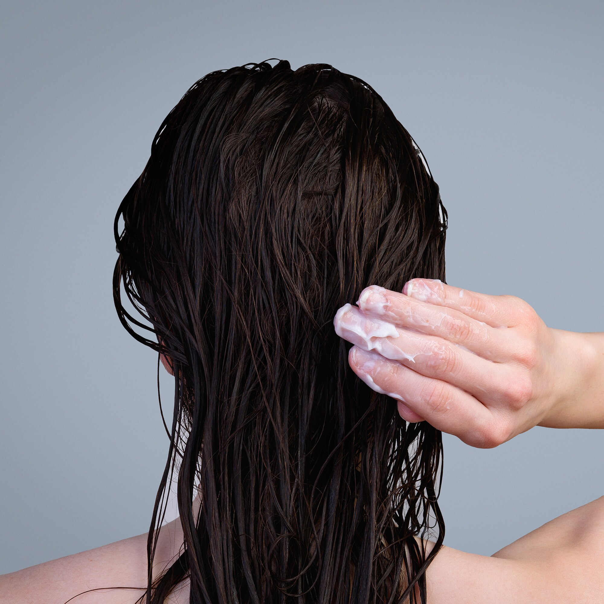 Back view of a woman applying hair treatment to long, dark, wet hair
