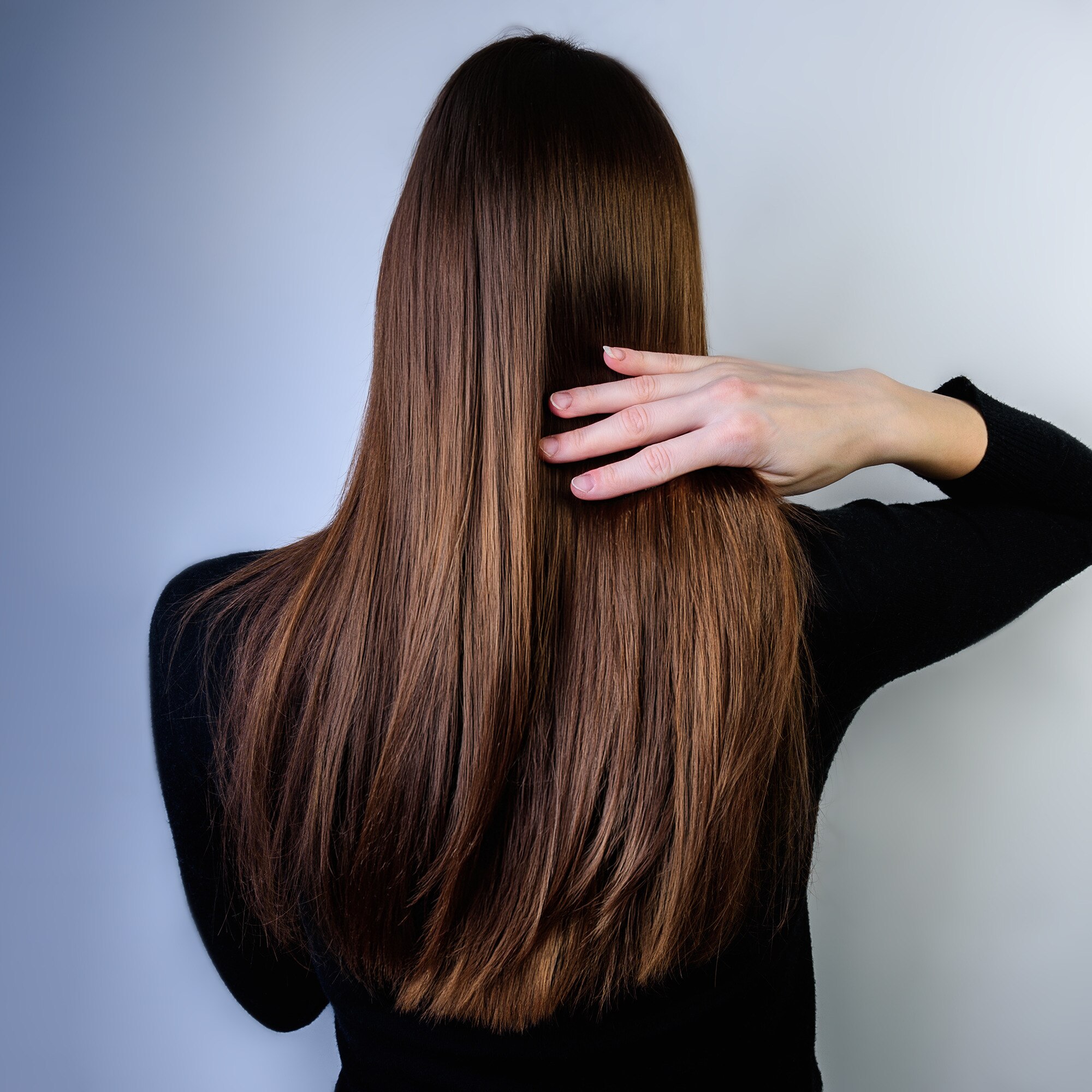 Back view of a woman running a hand over her long, brown glossy hair.