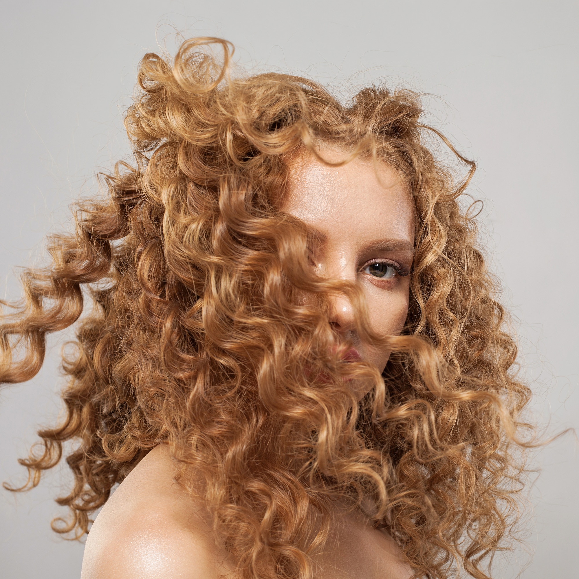 A woman with natural red-colored Type 3 curly hair with hair obscuring expression