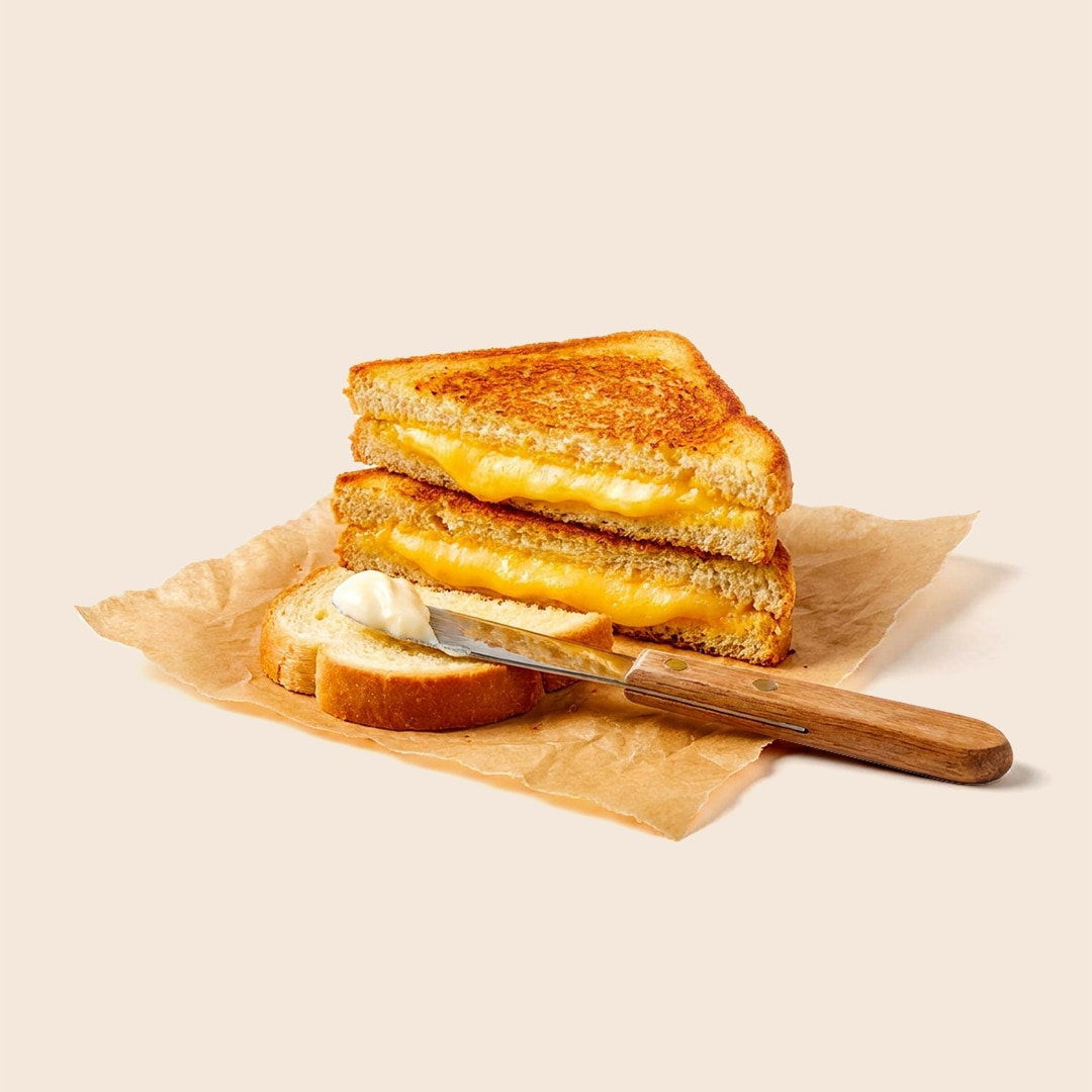 Toasted Wisconsin grilled cheese sandwich, cut in half with melted cheese pulling apart, next to a butter knife.