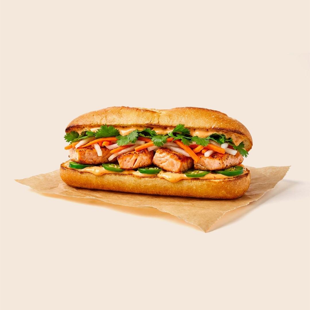 Salmon banh mi sandwich with pickled carrots, daikon, cilantro, jalapeños, and spicy mayo on a baguette.