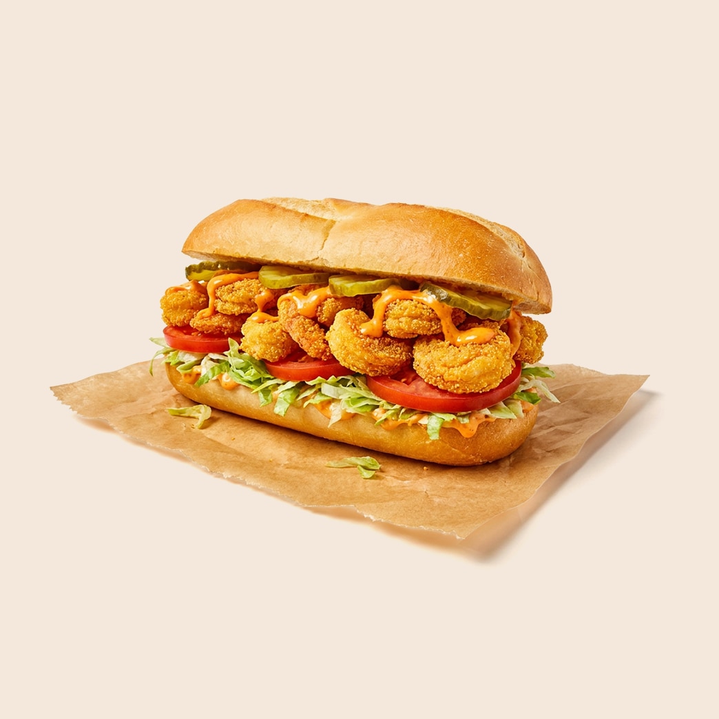 Crispy fried shrimp po' boy on a baguette with lettuce, tomato, pickles, and mayo-based remoulade sauce.