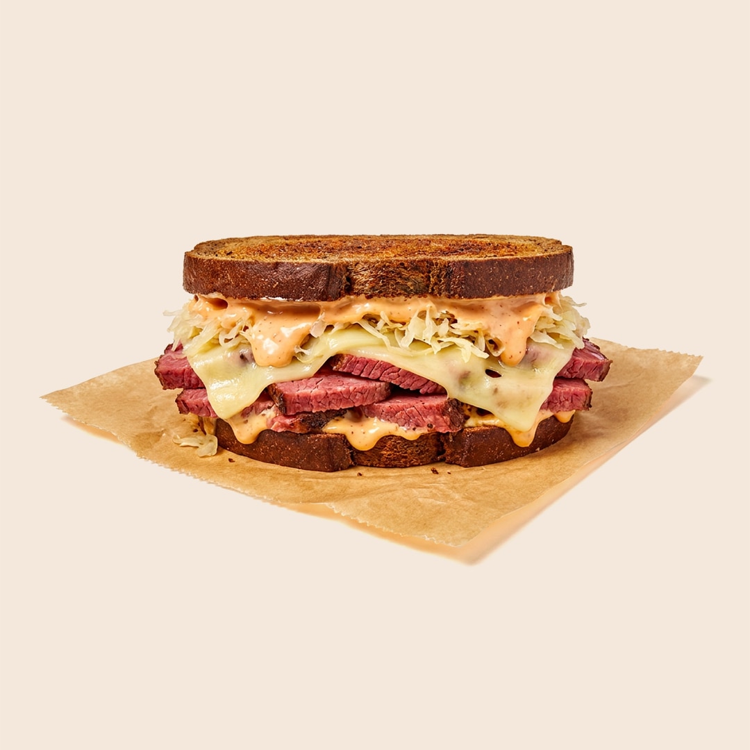 Classic Reuben sandwich with corned beef, melted Swiss cheese, sauerkraut, and mayo-based dressing on marbled rye bread.