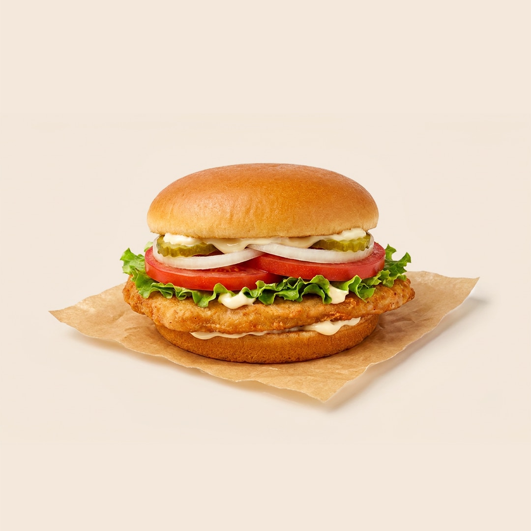Fried pork chop sandwich on a bun with lettuce, tomato, pickles, onions, and mayo.