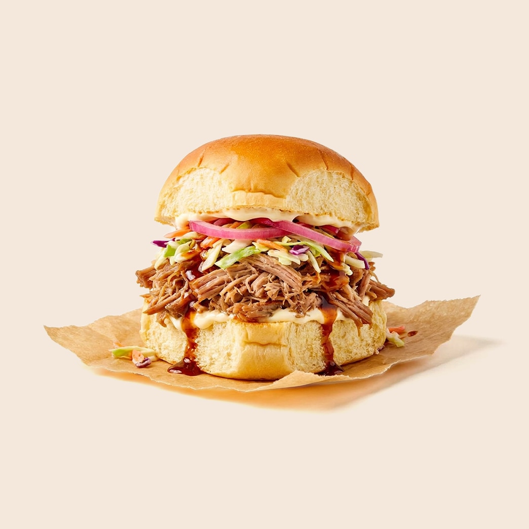 Shredded Kalua pork sandwich with coleslaw, red onion, barbecue sauce and mayo on a brioche bun.