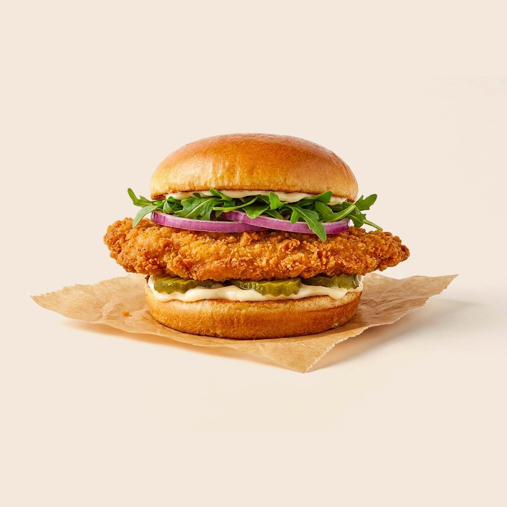 Giant crispy fried pork tenderloin sandwich with lettuce, onions, tomato, pickles, and mayo on a bun.