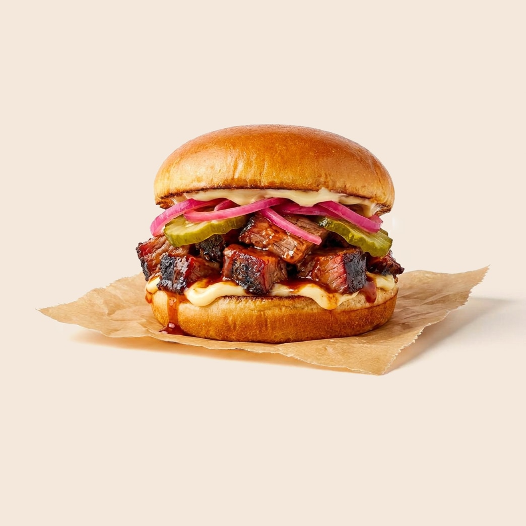 BBQ burnt ends sandwich with pickles, pickled red onions, barbecue sauce and mayo on a brioche bun.