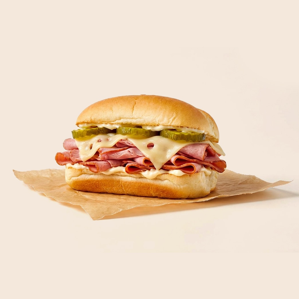 Sliced ham sandwich with melted Swiss cheese pickles and mayo on a long roll.