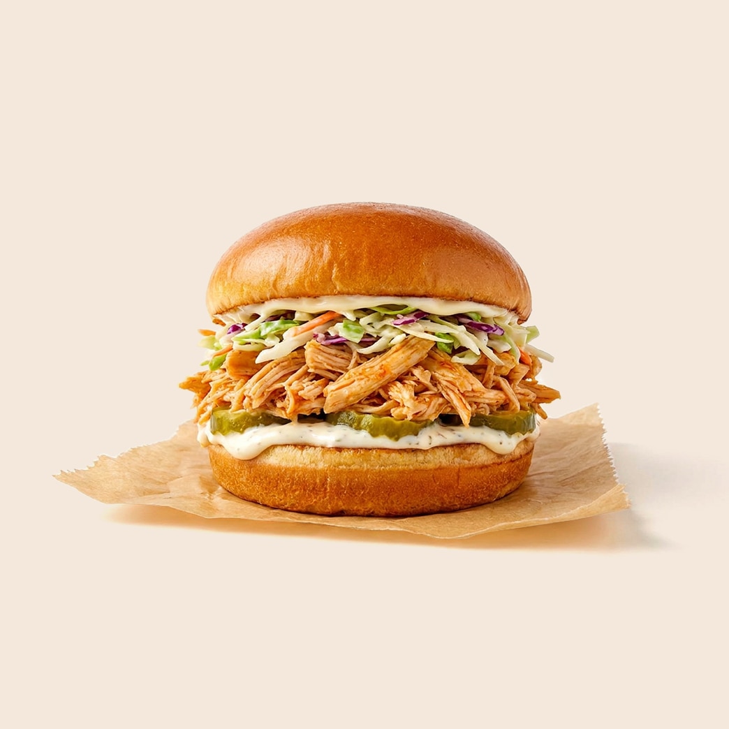 Pulled chicken sandwich topped with coleslaw with pickles and mayonnaise on a brioche bun. 
