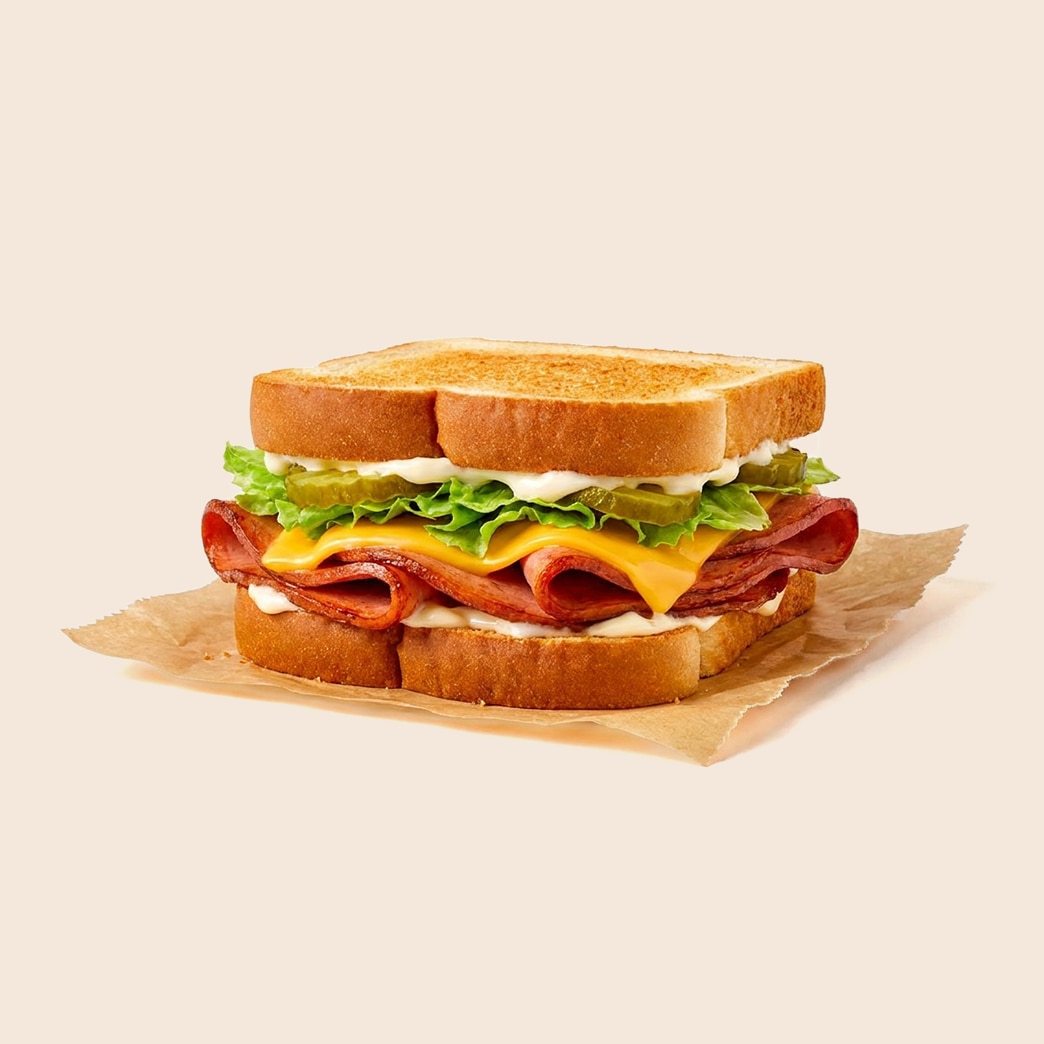 Fried bologna and cheese sandwich with lettuce, pickles, and mayo on toasted white bread. 