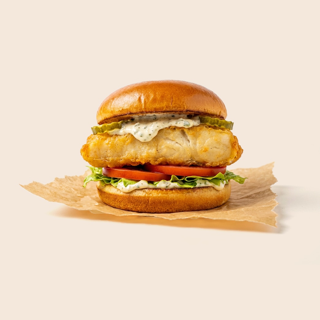 Fried halibut sandwich with lettuce, tomato, pickles, and mayo-based tartar sauce on a brioche bun.