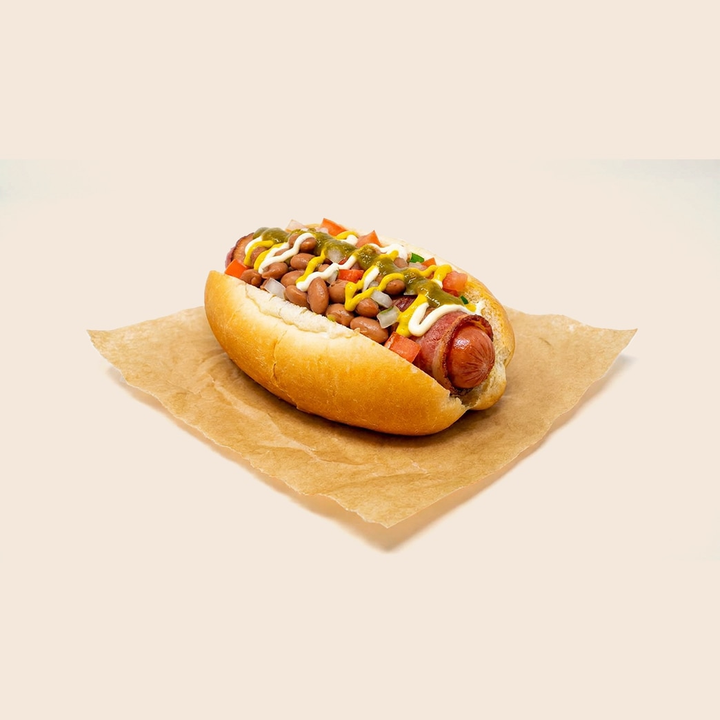 Bacon-wrapped Sonoran hot dog topped with pinto beans, onions, tomatoes, mustard, mayo, and green salsa. 