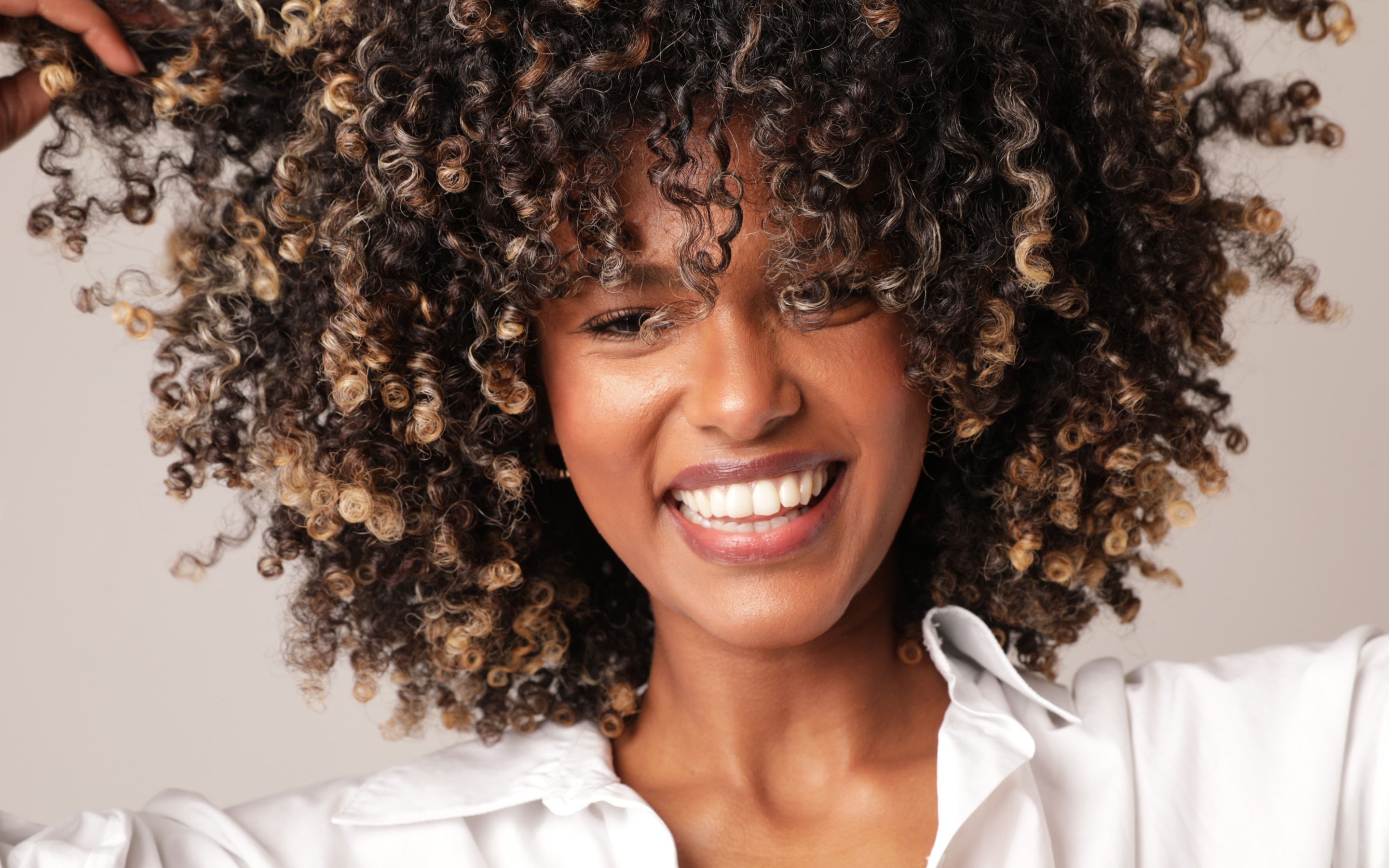 A woman in a white shirt playfully pulls out her type 4 coily hair