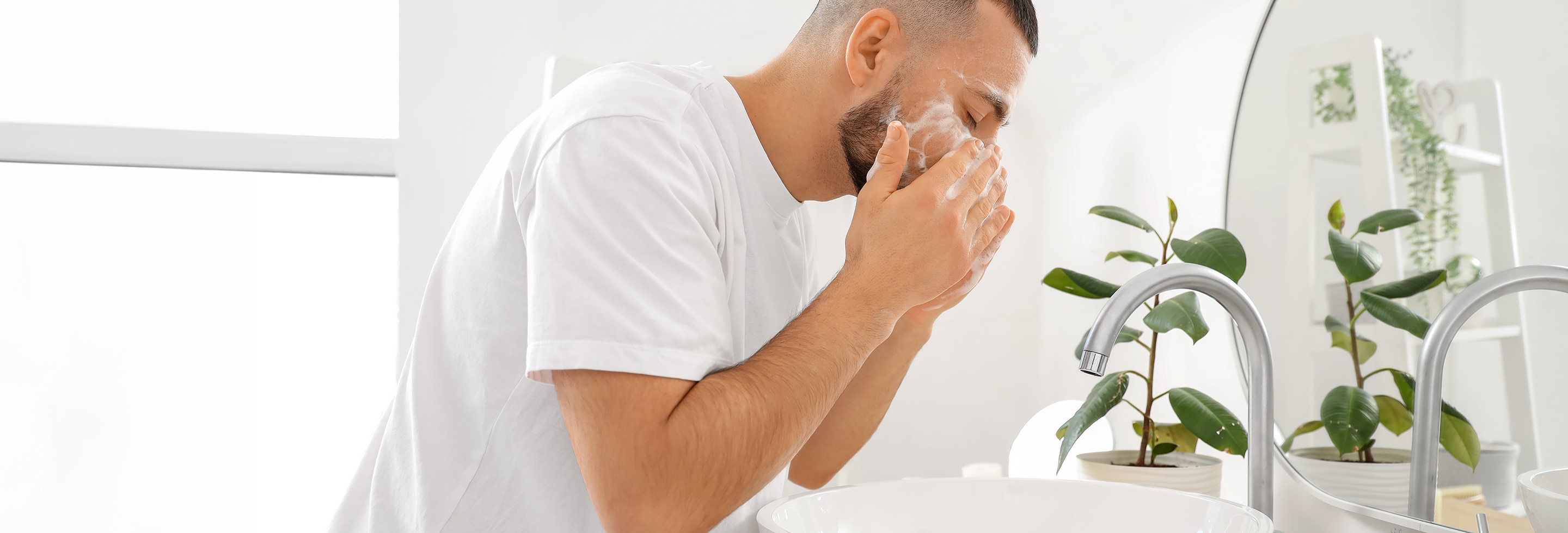 Young man with dry skin washing his face with a Dove&nbsp;Men+Care&nbsp;cleansing bar near sink in bathroom&nbsp;
