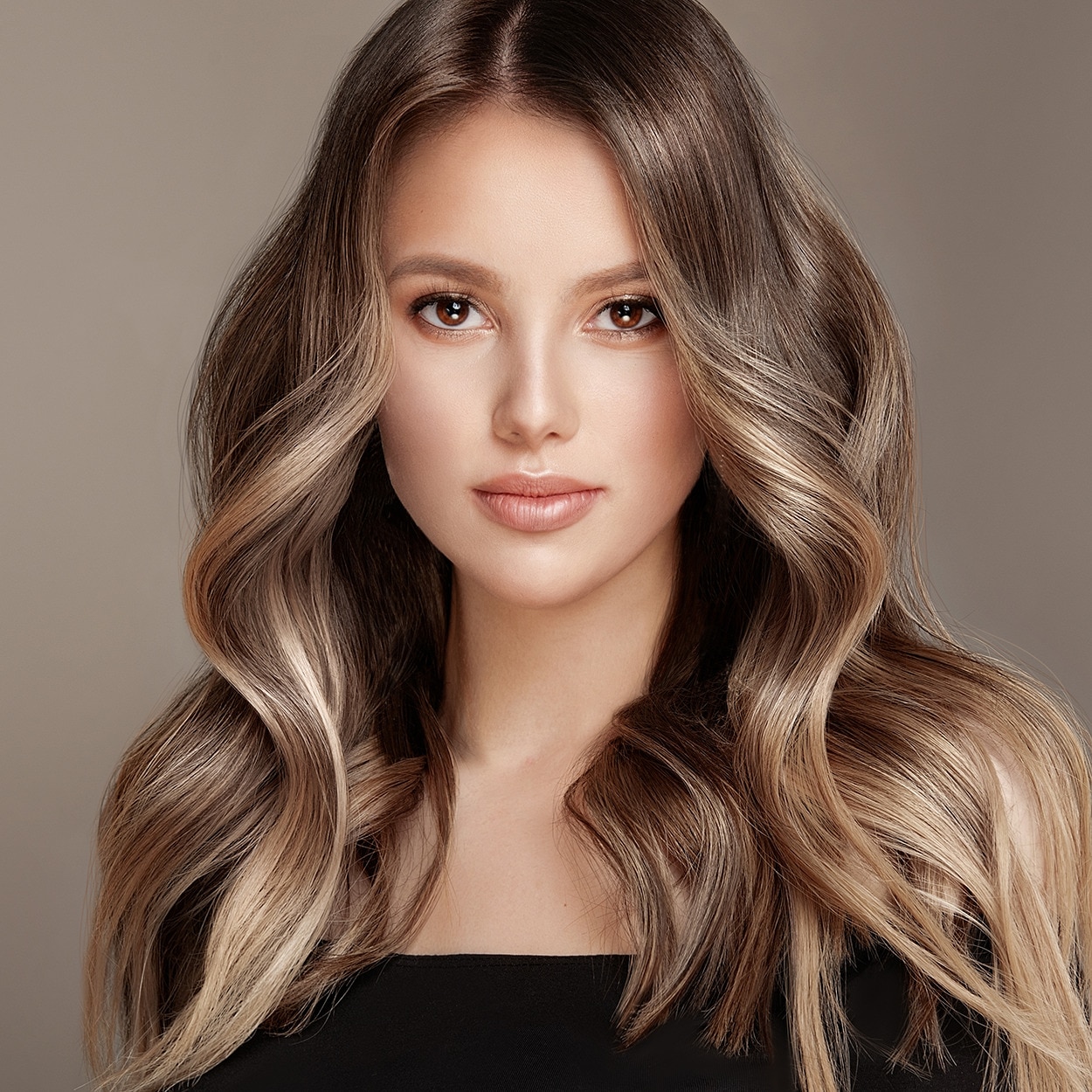 A woman with long, brown-blonde hair that falls in sculpted waves across her shoulders, wearing a sequinned top