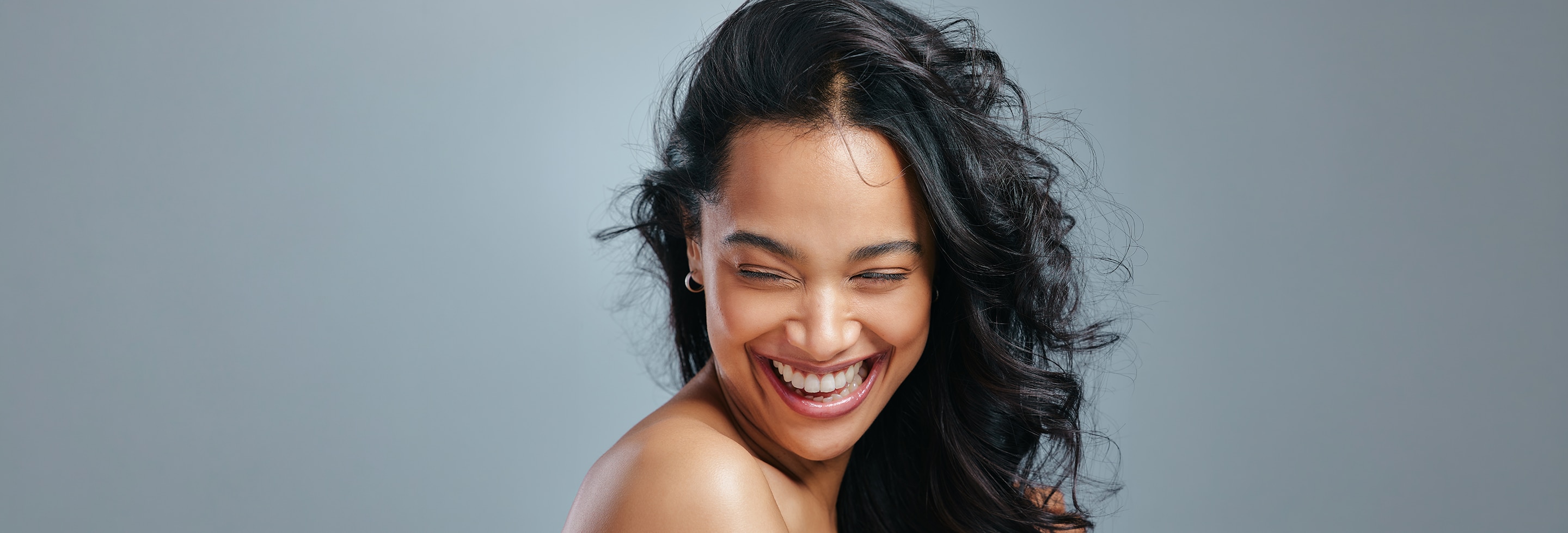 Woman with long black hair smiling, against grey background.