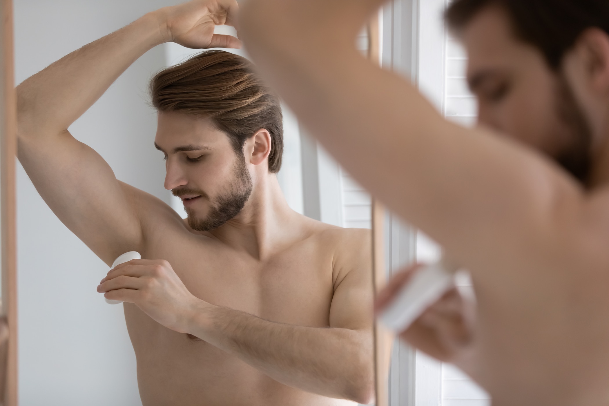 Young guy applying deodorant in the bathroom and wondering why it clumps
