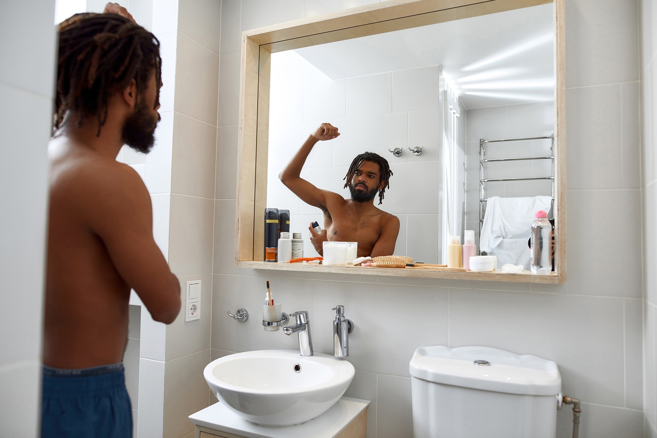 Young African-American man using antiperspirant in his bathroom wondering if he should switch to aluminum-free deodorant