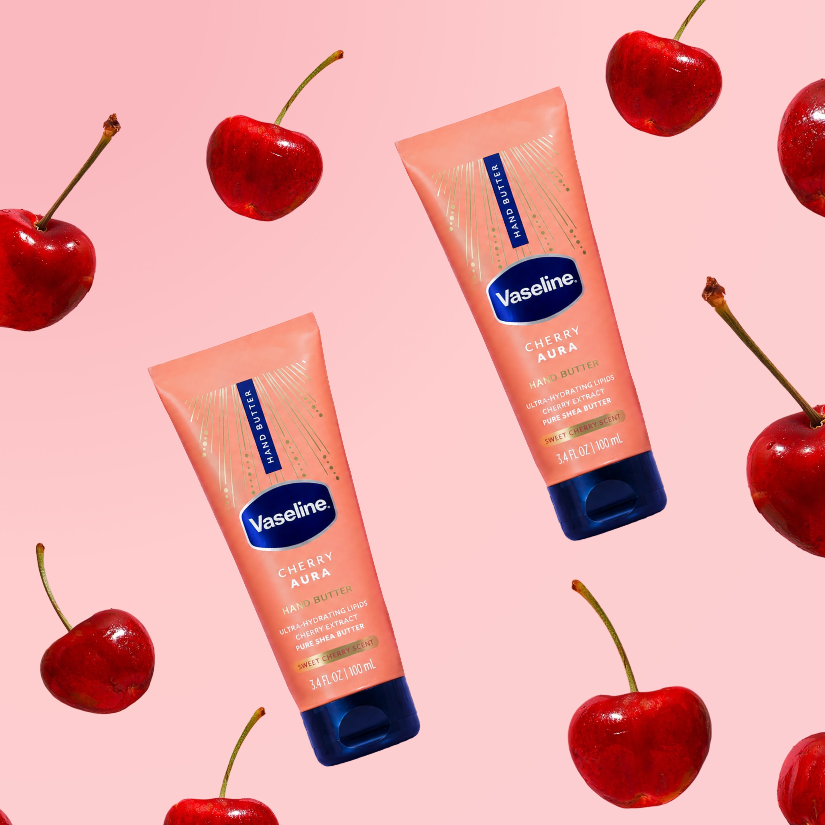 Two tubes of Vaseline Cherry Aura Hand Butter float among bright red cherries on a soft pink background.