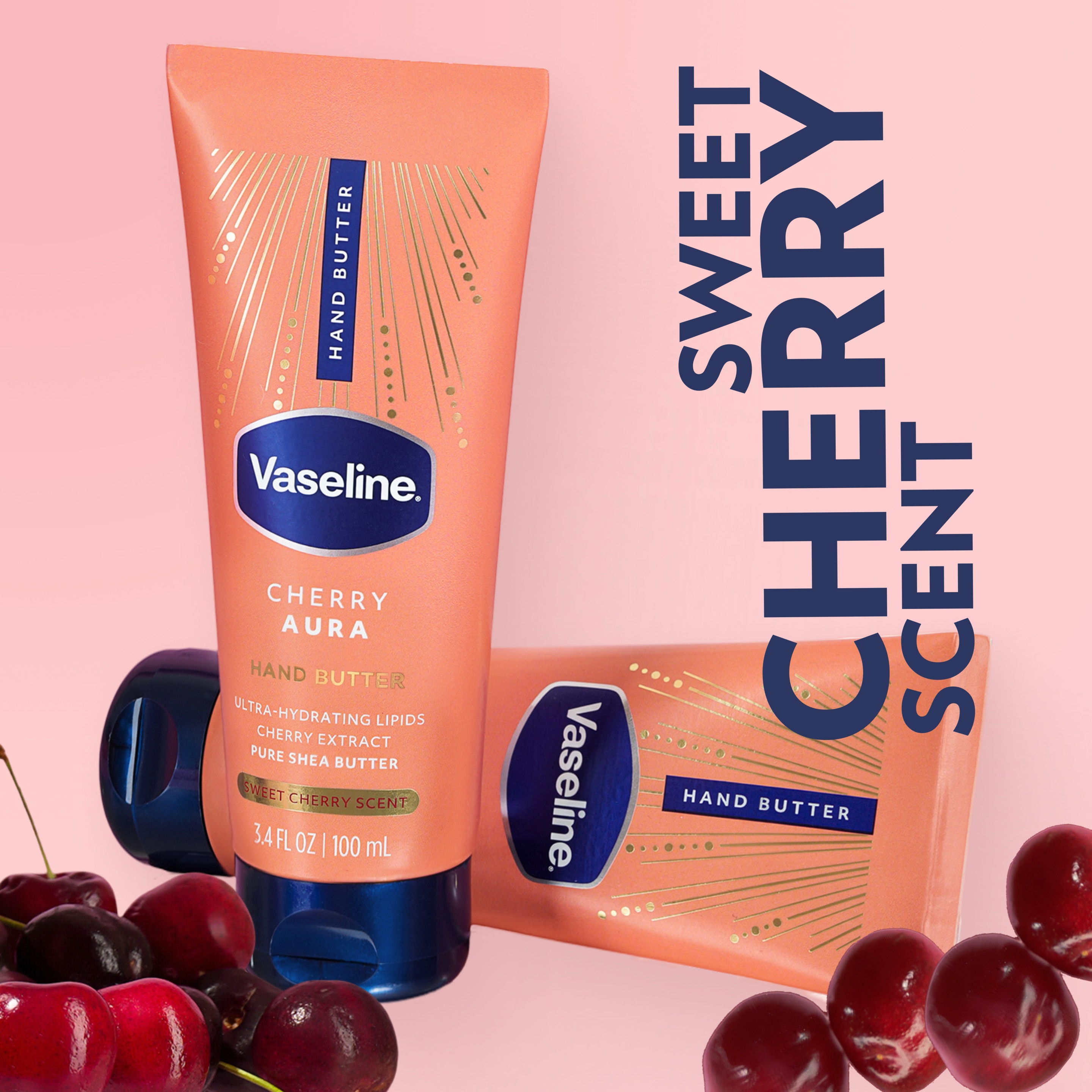 Two tubes of Vaseline Cherry Aura Hand Butter are displayed with fresh cherries on a pink background with text