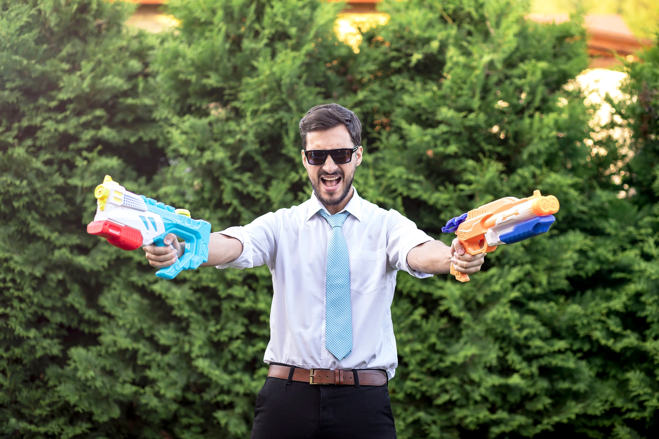 Guy in work clothes playing with water guns to cool down in summer